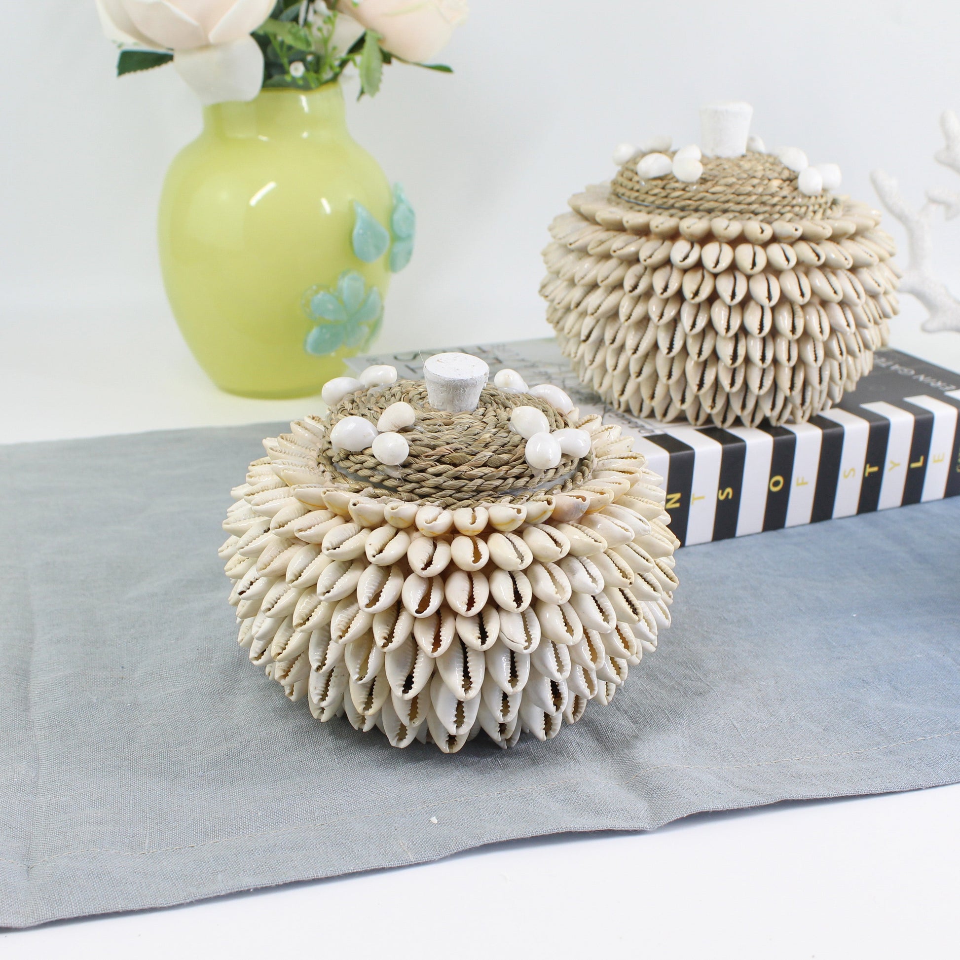 Set of handmade layered cowrie shell boxes in different sizes, arranged on soft blue table runner.