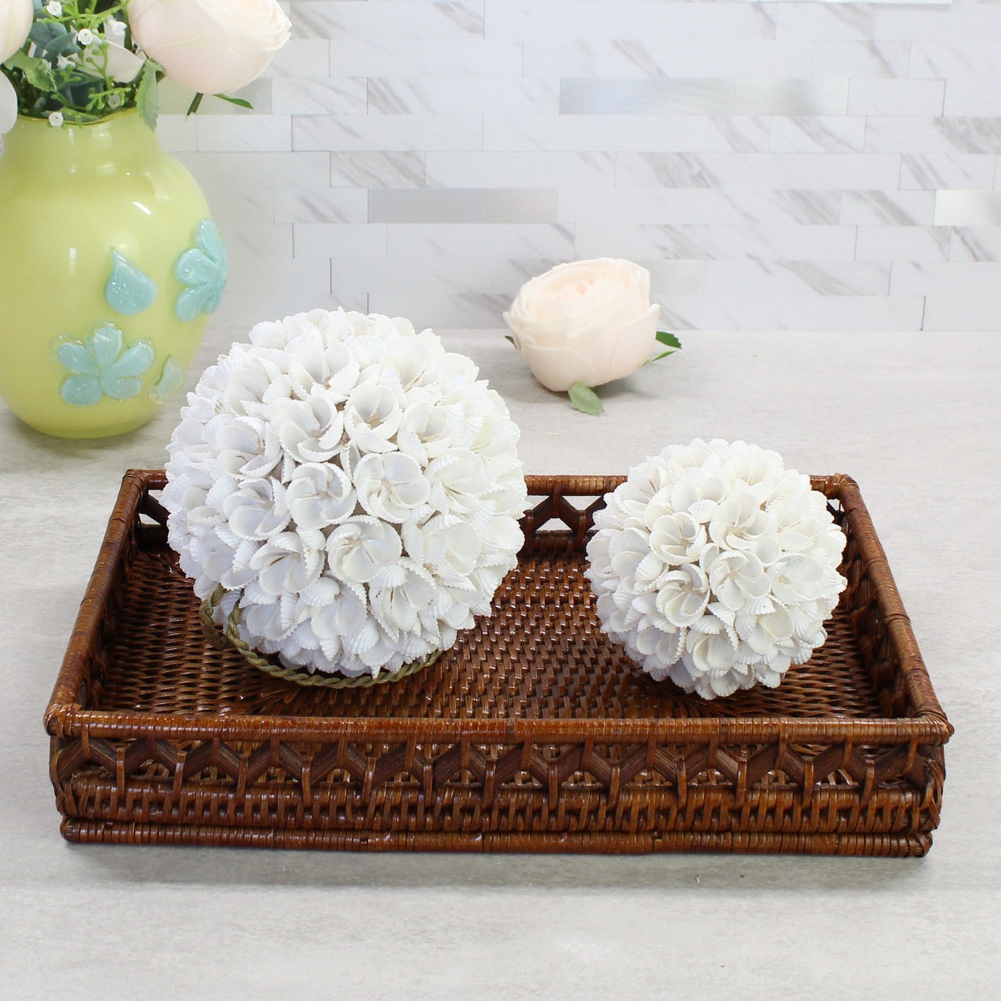 Eco Handcraft handmade seashell blossom balls in two sizes styled on a rattan tray with ivory roses and soft neutral tones for coastal home decoration.
