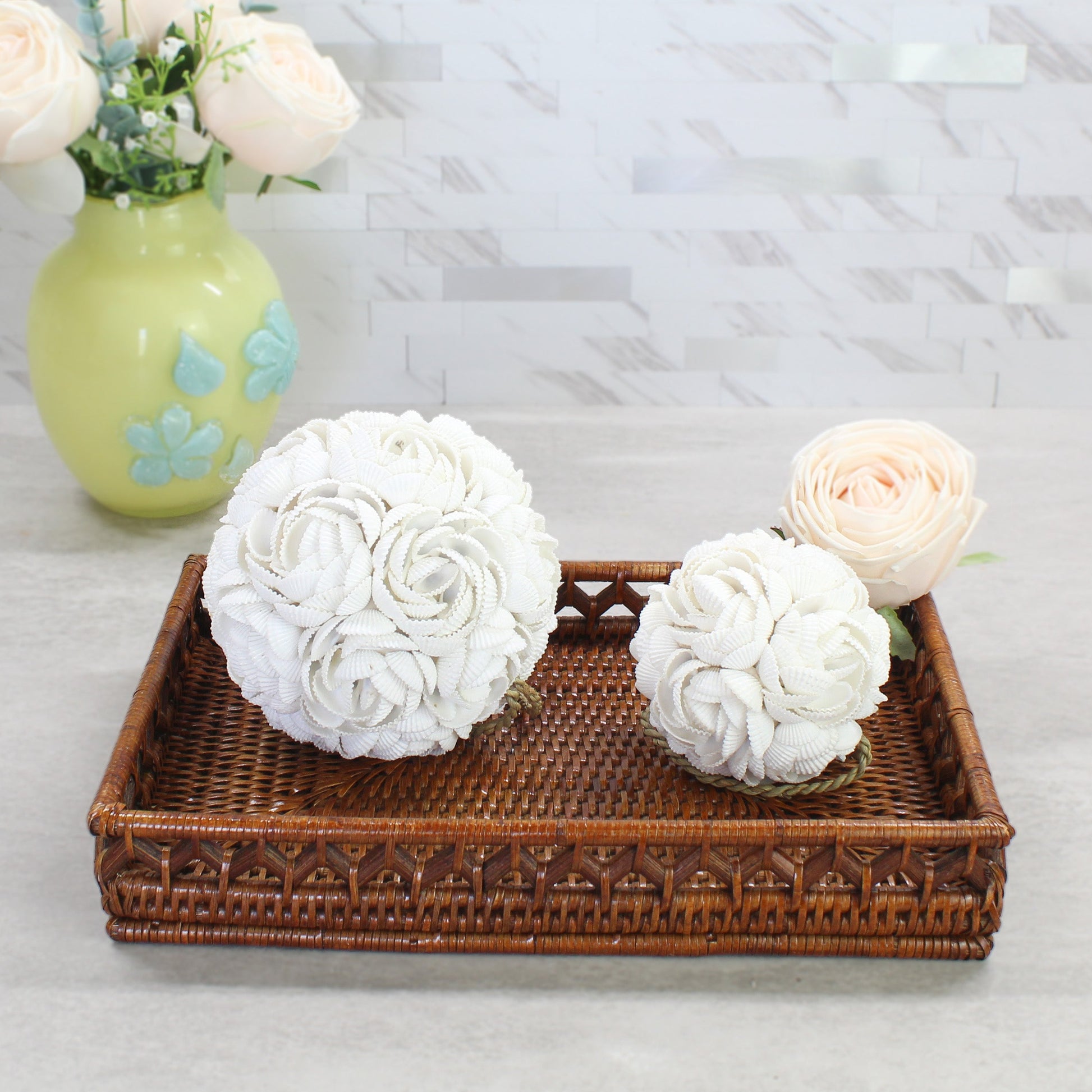 Eco Handcraft handmade seashell rose balls in two sizes styled on a rattan tray with ivory roses and soft neutral tones for coastal home decoration.