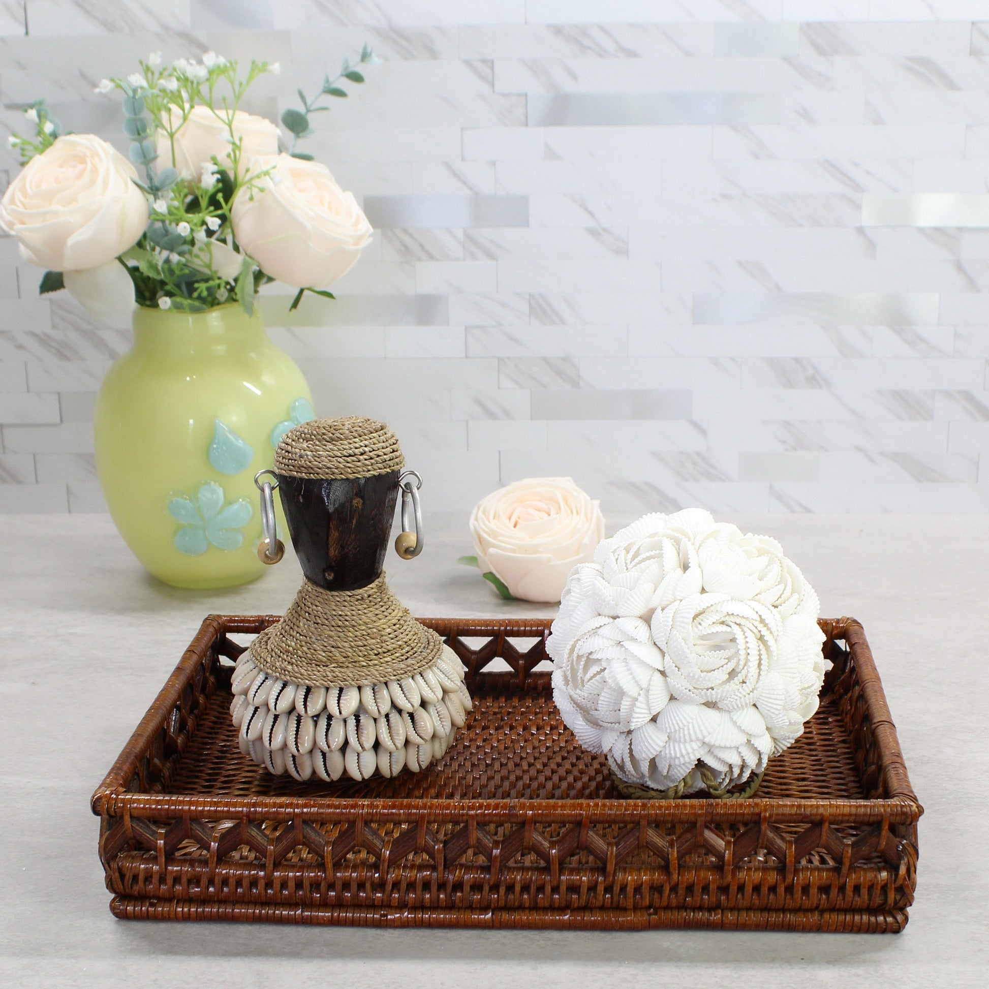 Handcrafted white seashell rose ball displayed on a woven tray beside a Bali shell statue, showing artisan coastal craftsmanship and natural texture.