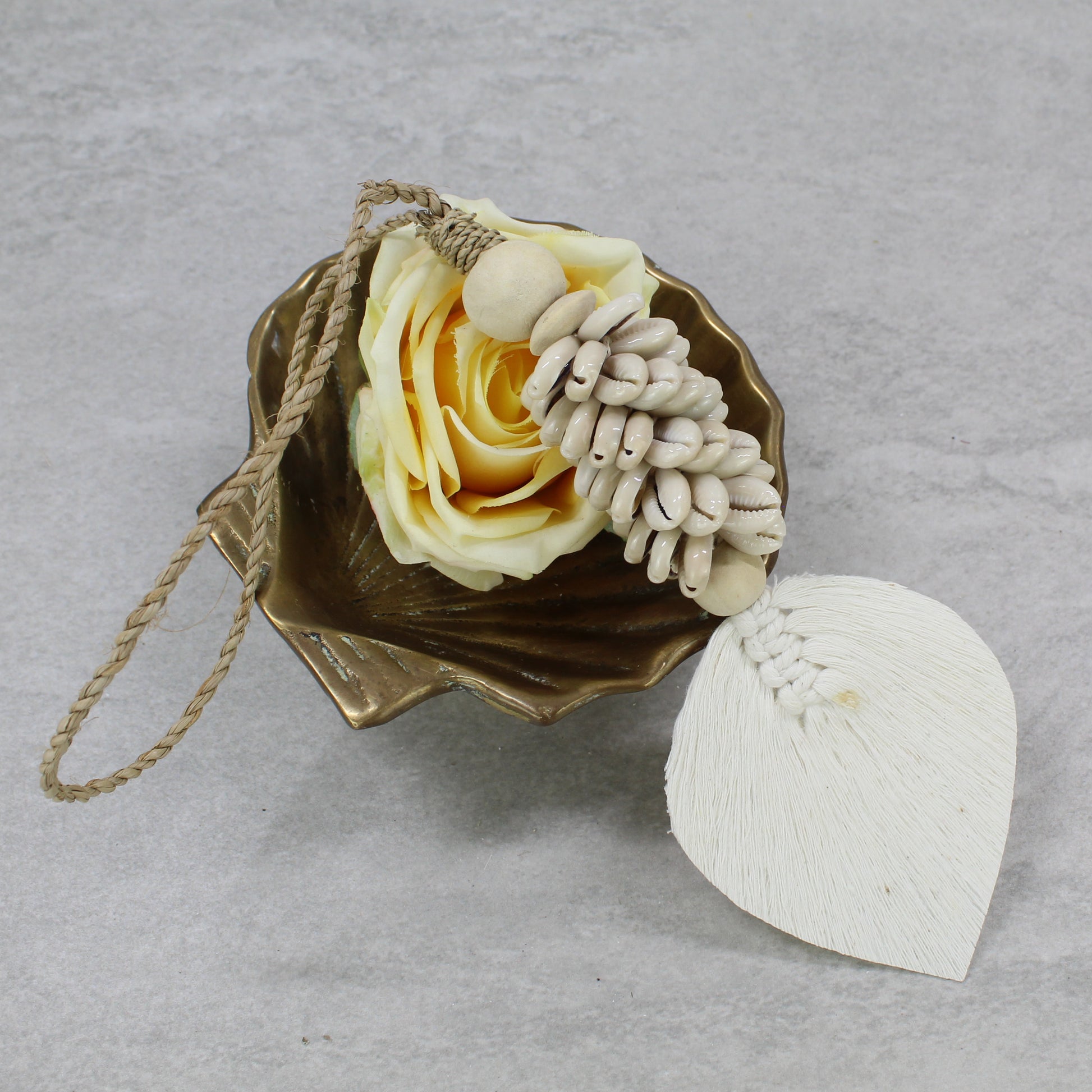 Handmade beige shell tassel with macramé cotton leaf and jute hanger styled with yellow rose in bowl decor setup