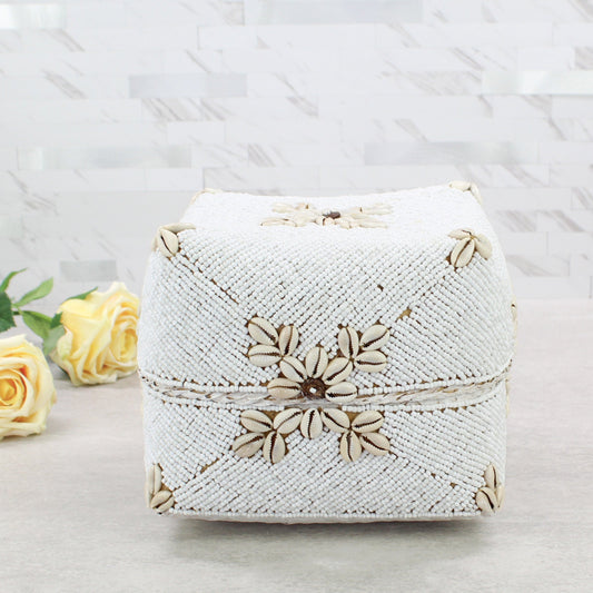 Large handmade white beaded cowrie shell decorative storage box displayed with yellow roses on neutral countertop.