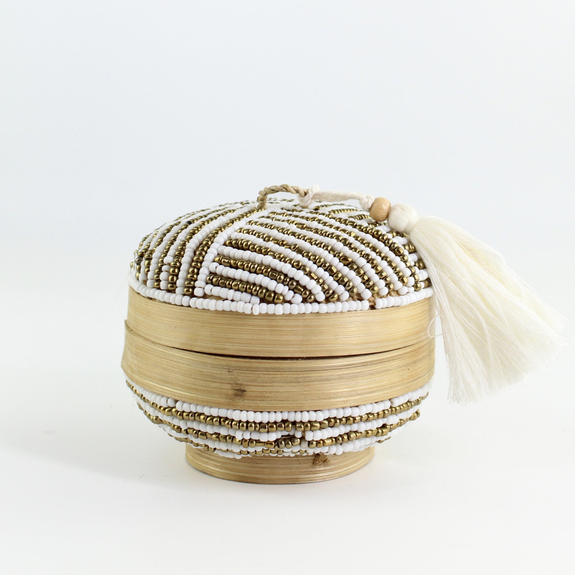 Close-up of handmade white and gold linear beaded bamboo box with tassel on white background