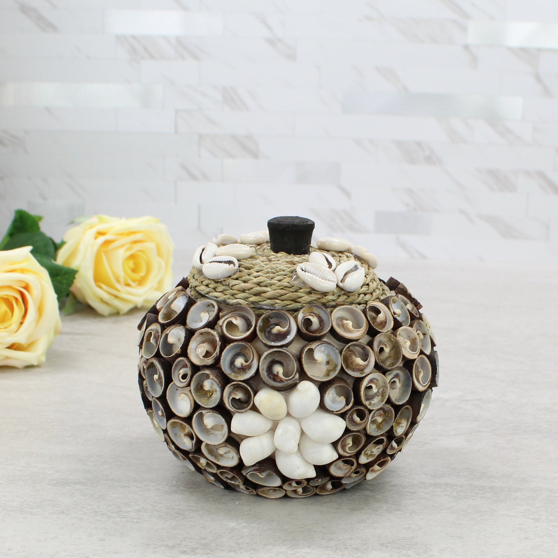Medium cowrie seashell storage box with rope lid, artisan handmade, styled with floral décor for coastal home or cottage display.
