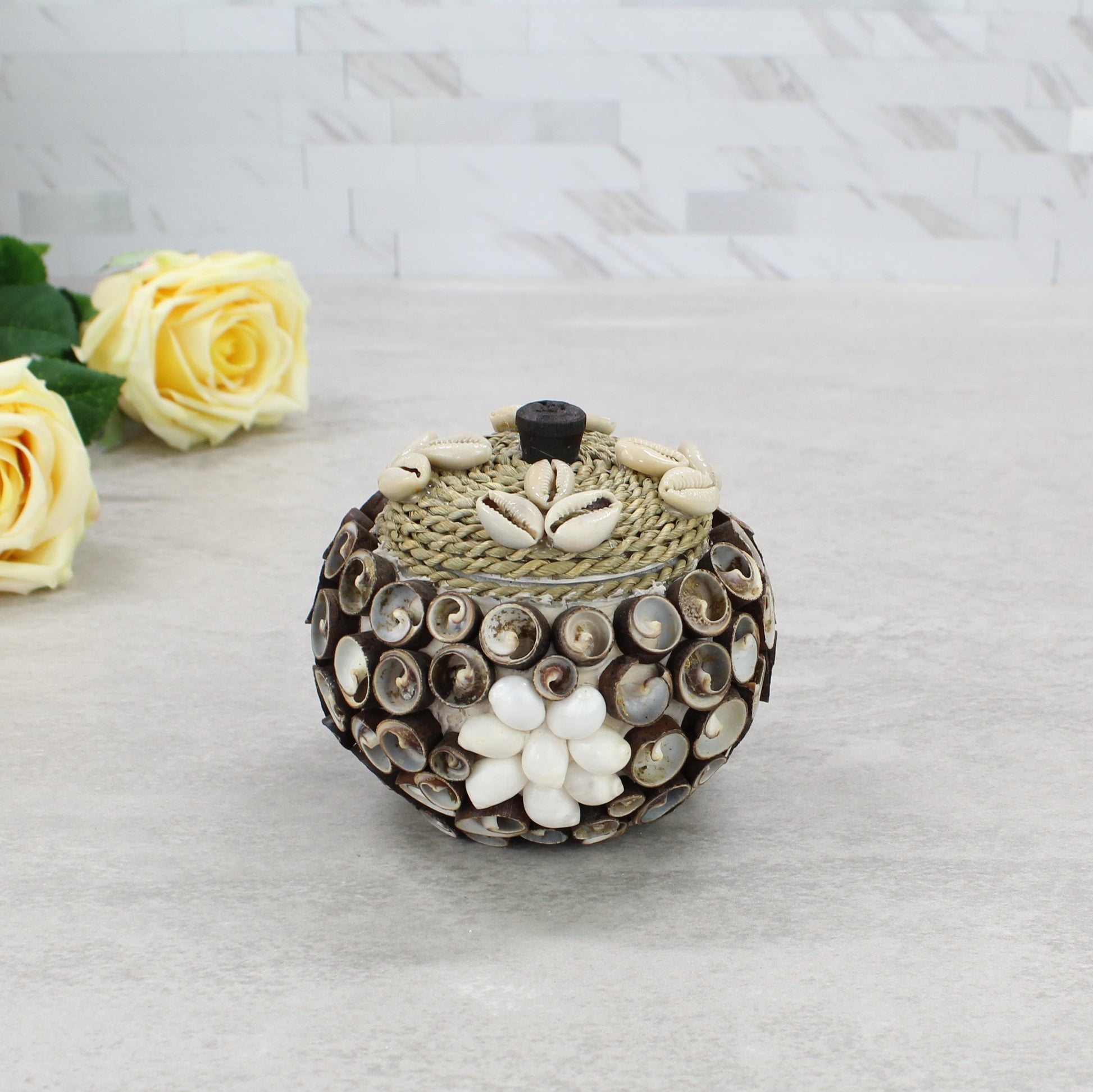 Small cowrie seashell storage box with rope lid, artisan handmade, styled with floral décor for coastal home or cottage display.
