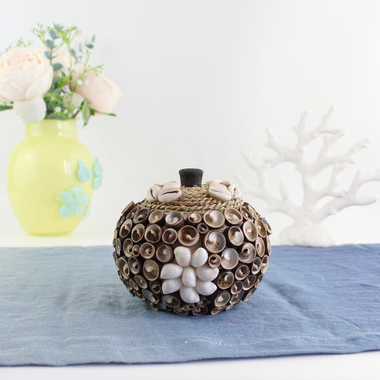 Handmade cowrie seashell storage box with rope lid, artisan handmade, styled with floral décor for coastal home or cottage display.
