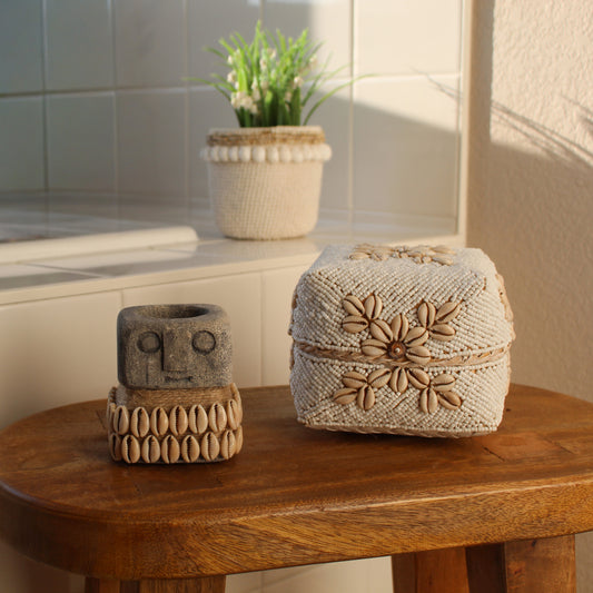 Handmade beaded cowrie shell box styled with coastal décor and seagrass candle holder on wooden stool in sunlight.