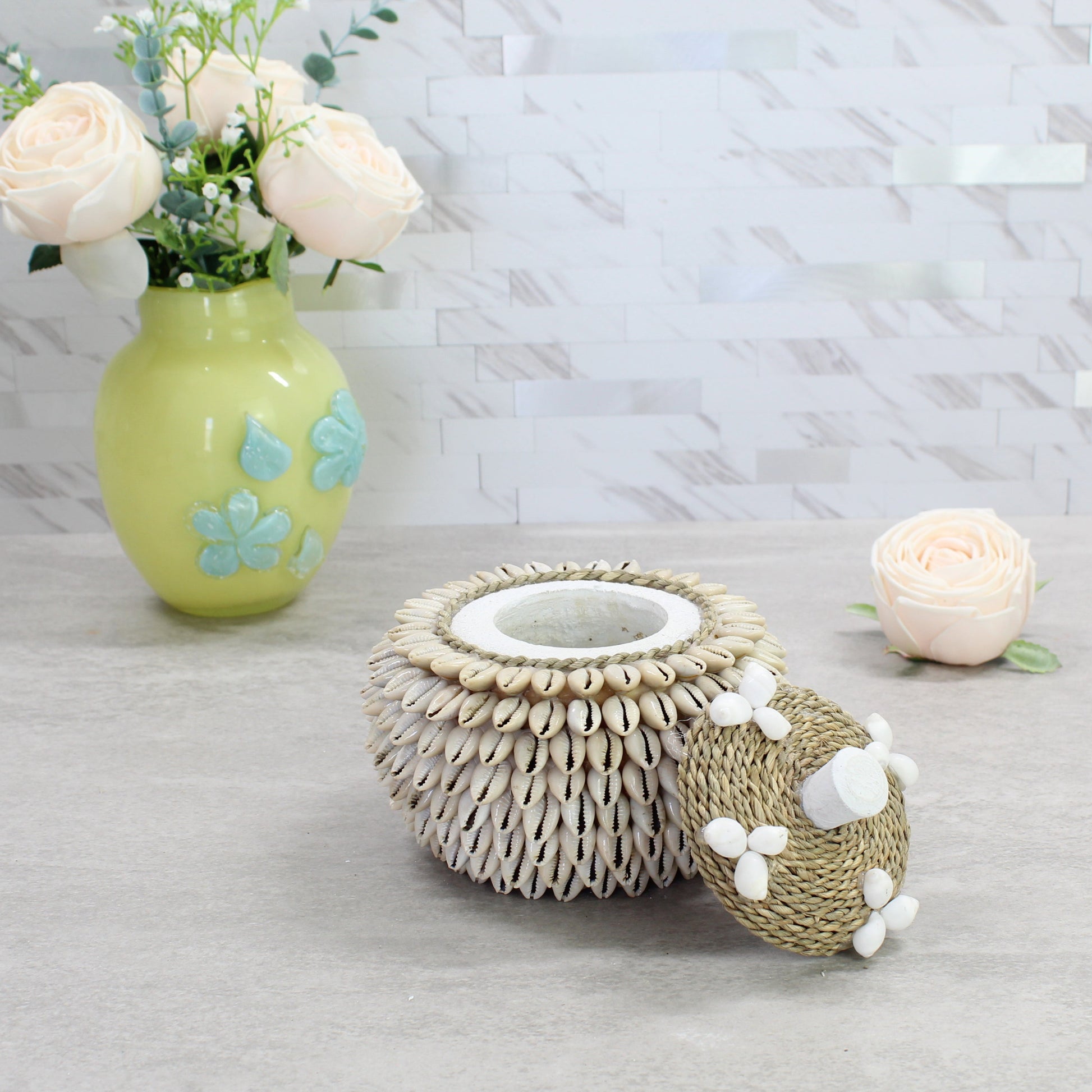 Coastal-inspired handmade cowrie shell box with open lid, styled beside flowers and decorative vase.