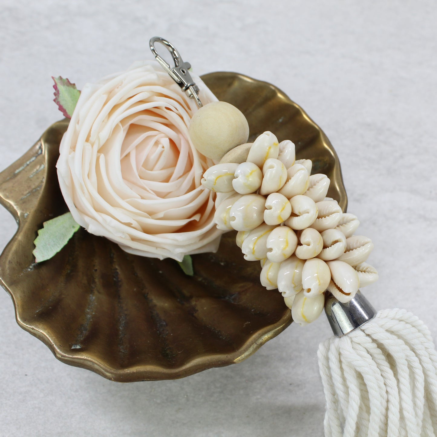 Close-up of real natural seashells and wooden bead on handmade tassel key ring, eco-friendly beach-inspired design.