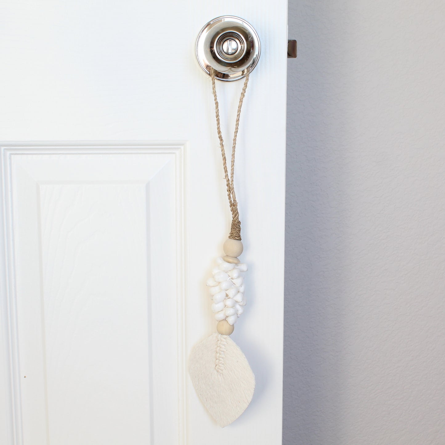 White beaded seashell tassel with braided jute loop used as boho curtain tieback on white door handle