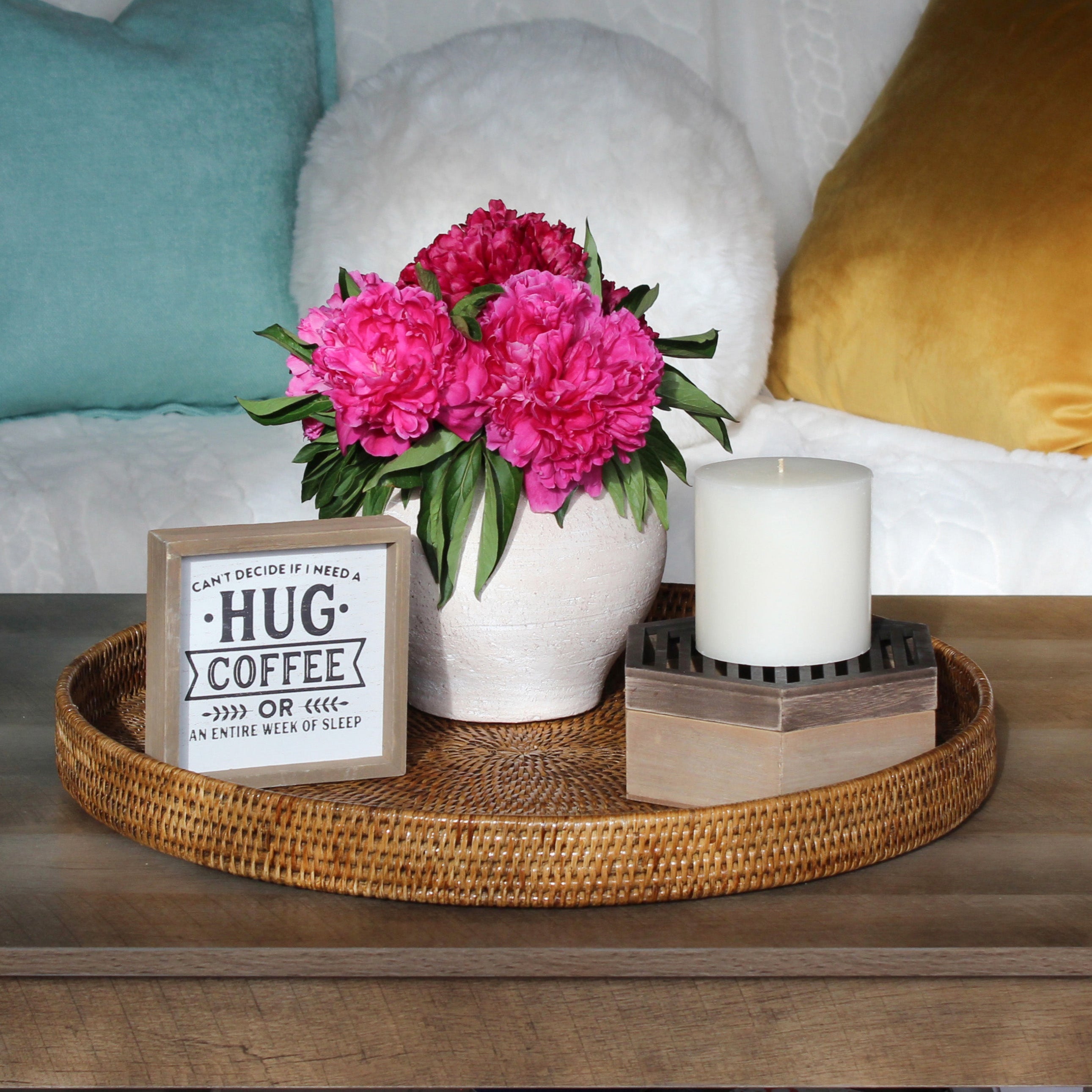 Eco Handcraft round rattan tray styled with pink flowers, a candle, and cozy pillows on a wood coffee table