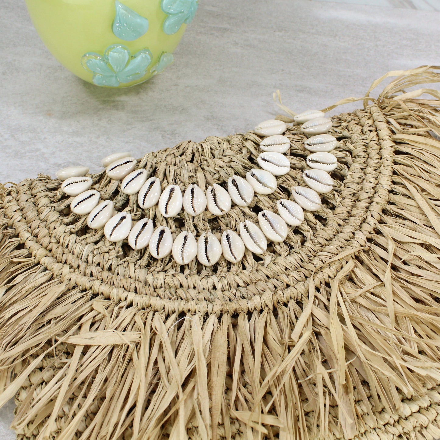 Handcrafted raffia clutch with two concentric rows of cowrie shells and raffia fringe — minimalist boho beach purse.