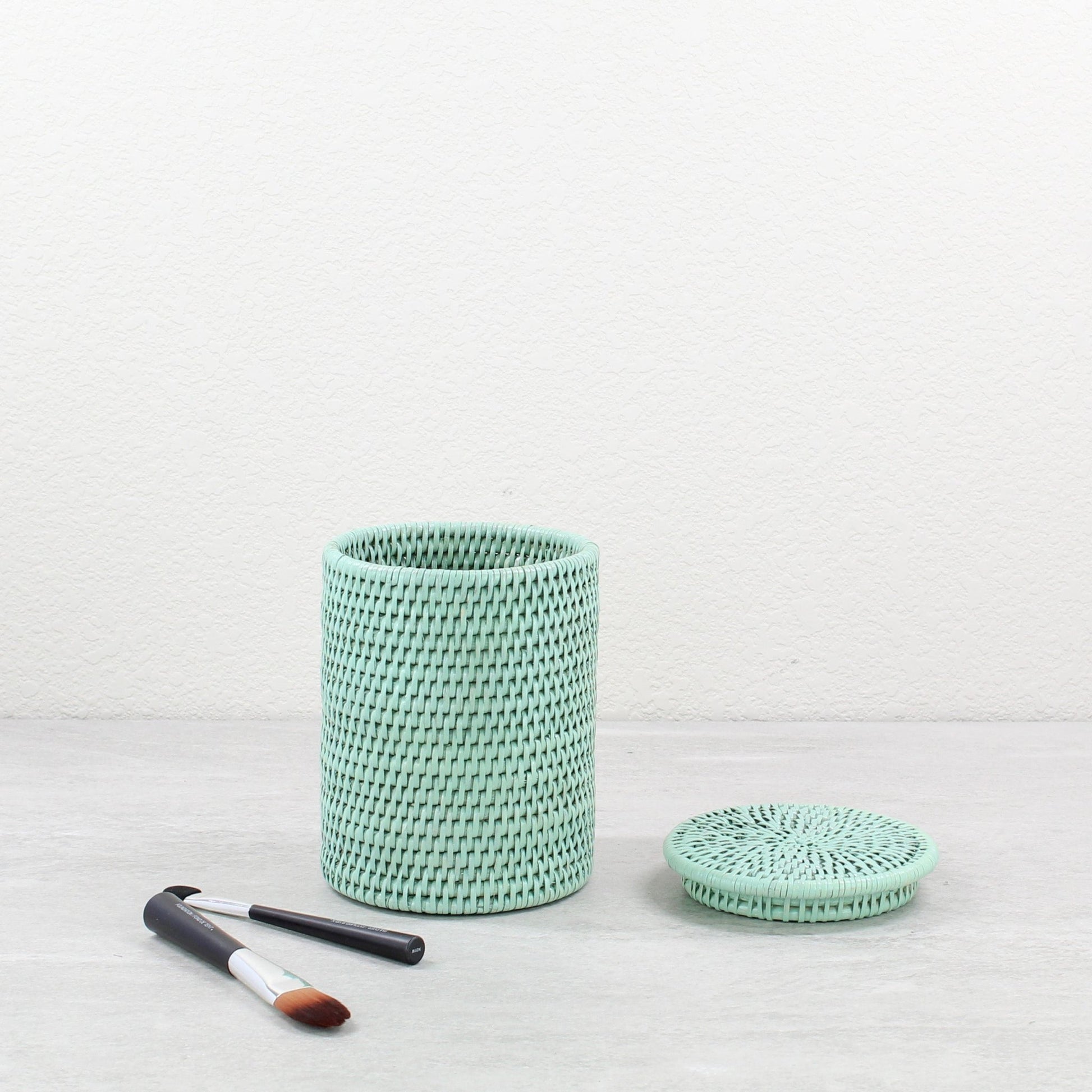 Sage leaf green woven rattan canister basket with a lid on a light background