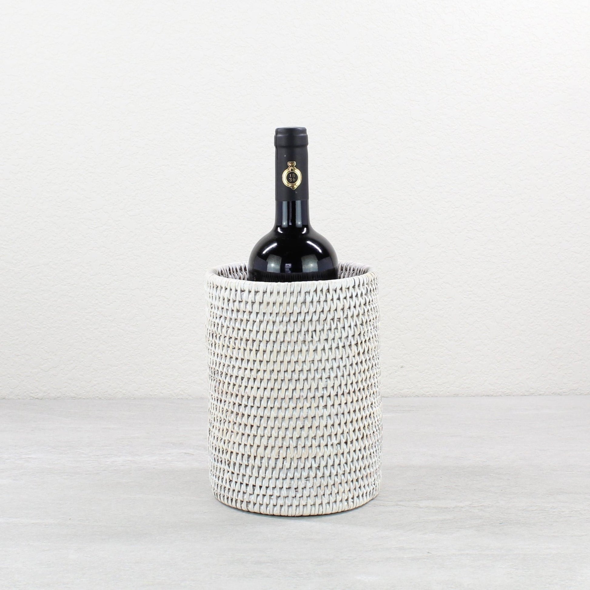 Handwoven whitewash rattan wine holder with a bottle of wine on a light gray background