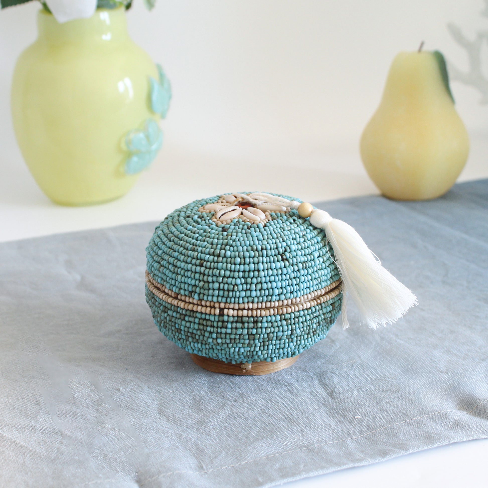 Handmade turquoise beaded seashell box with white tassel styled on linen table, coastal-inspired jewelry storage decor by ECO HANDCRAFT.