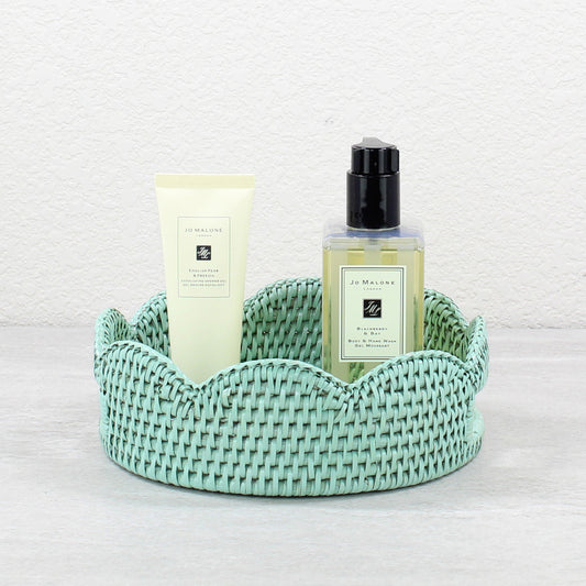 Sage Leaf Green woven rattan scalloped basket with two bottles of Jo Malone products on a stone surface.
