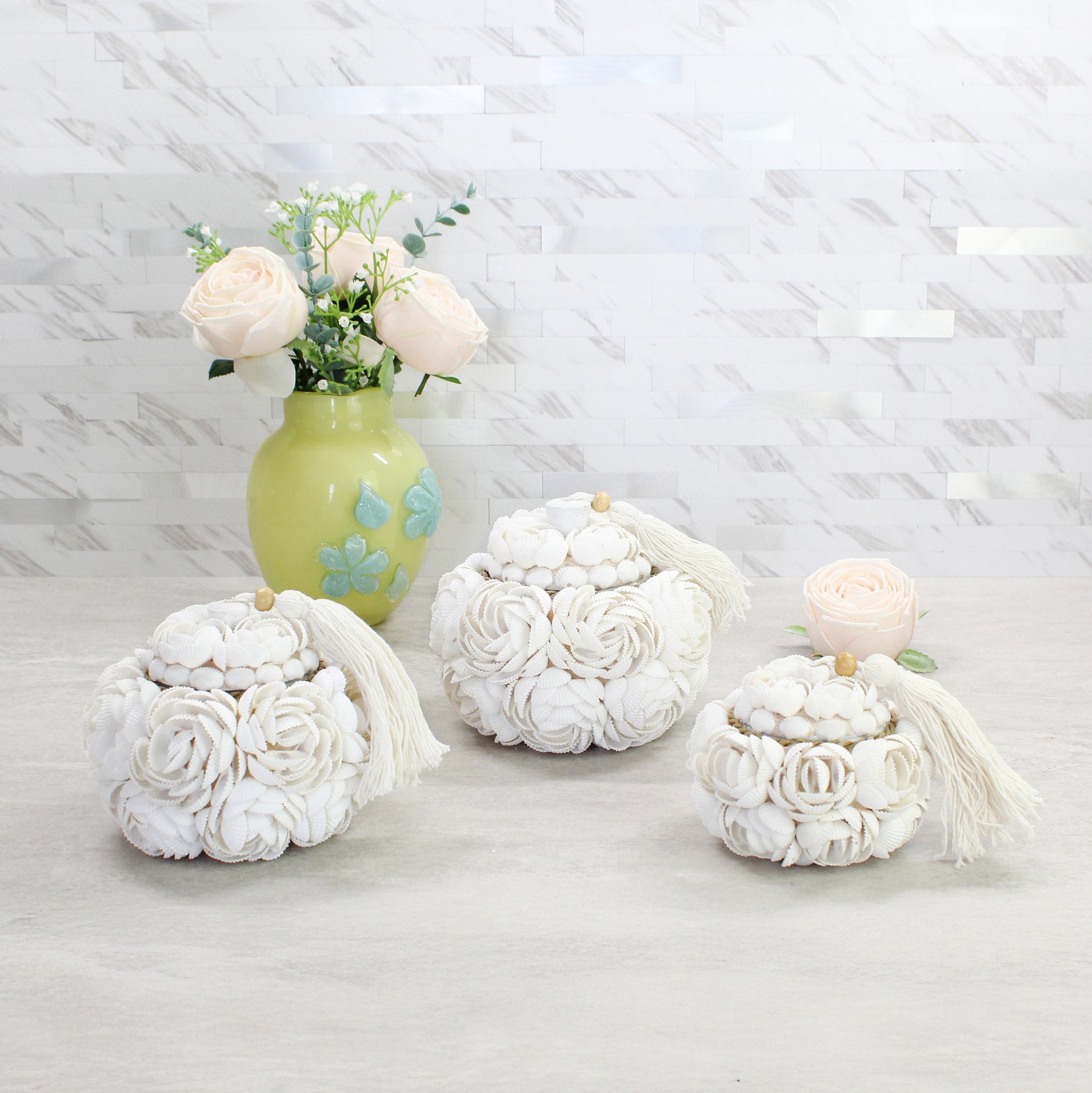 Set of three handmade seashell rose storage boxes with tassels in small, medium, and large sizes, displayed with a floral vase for coastal-inspired décor.