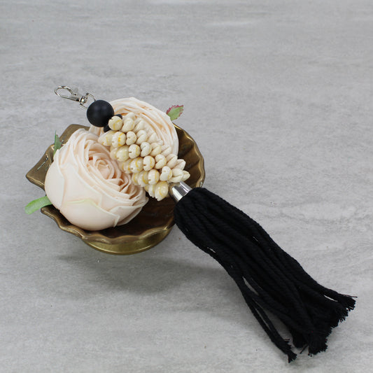 Natural sand seashell key ring with black cotton tassel and matte black bead displayed in brass dish with flower décor.