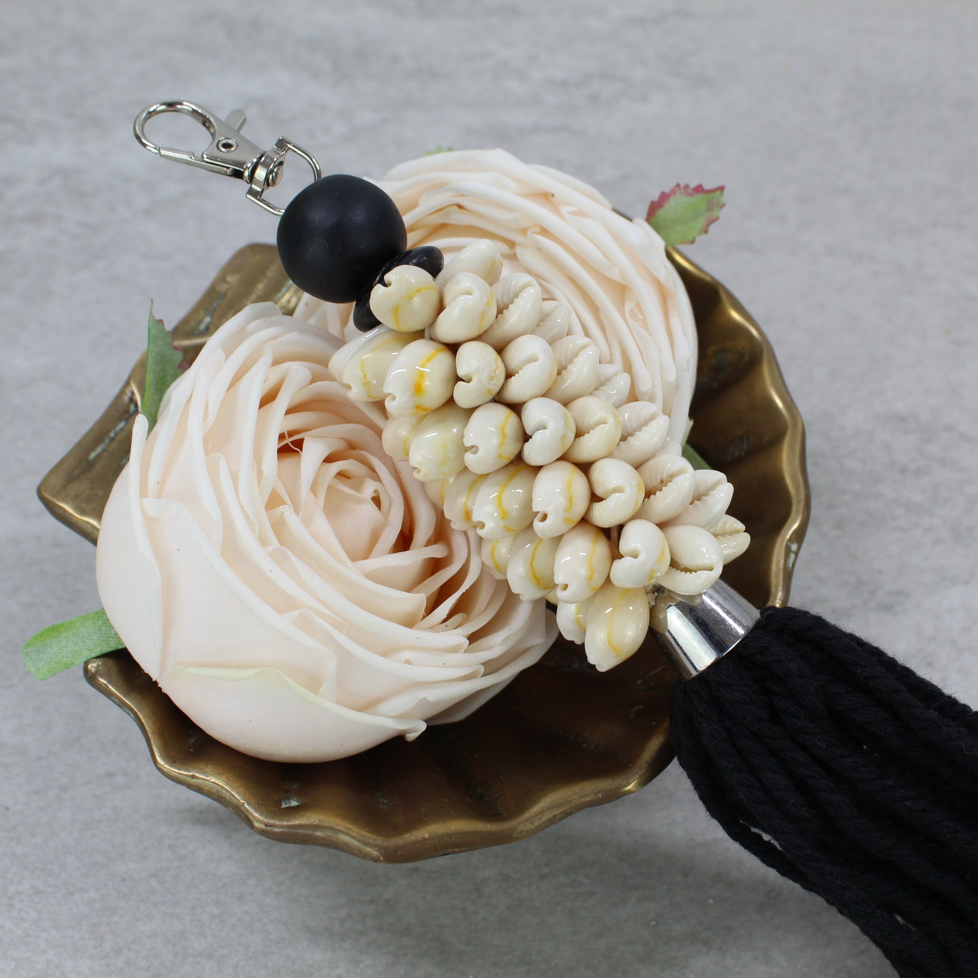 Close-up of natural seashell cluster and black bead on handmade black cotton tassel key ring, neutral coastal accessory.