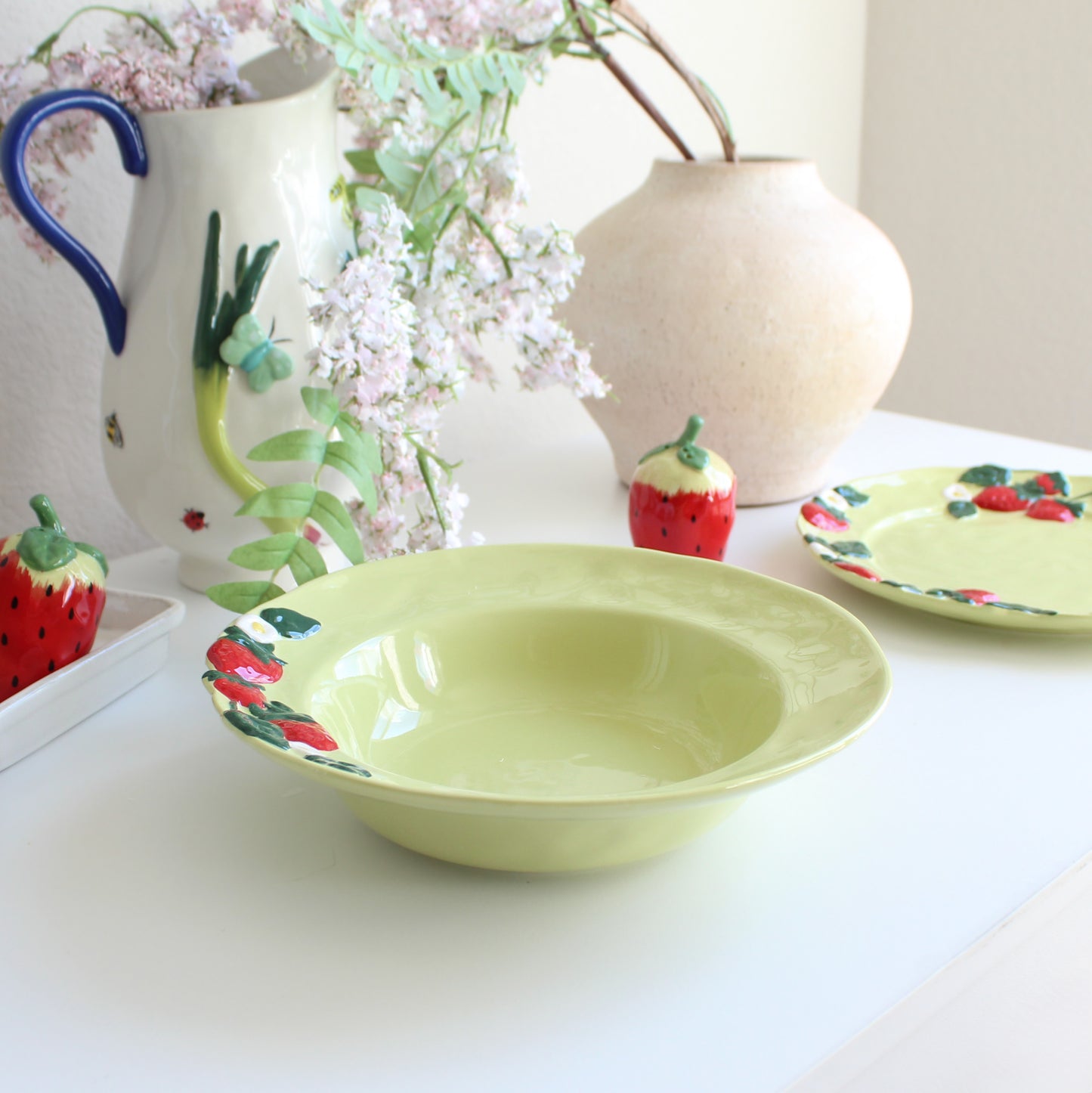 Strawberry-themed handpainted stoneware pasta bowl styled on table with matching dinnerware collection, plate, and salt & pepper shakers