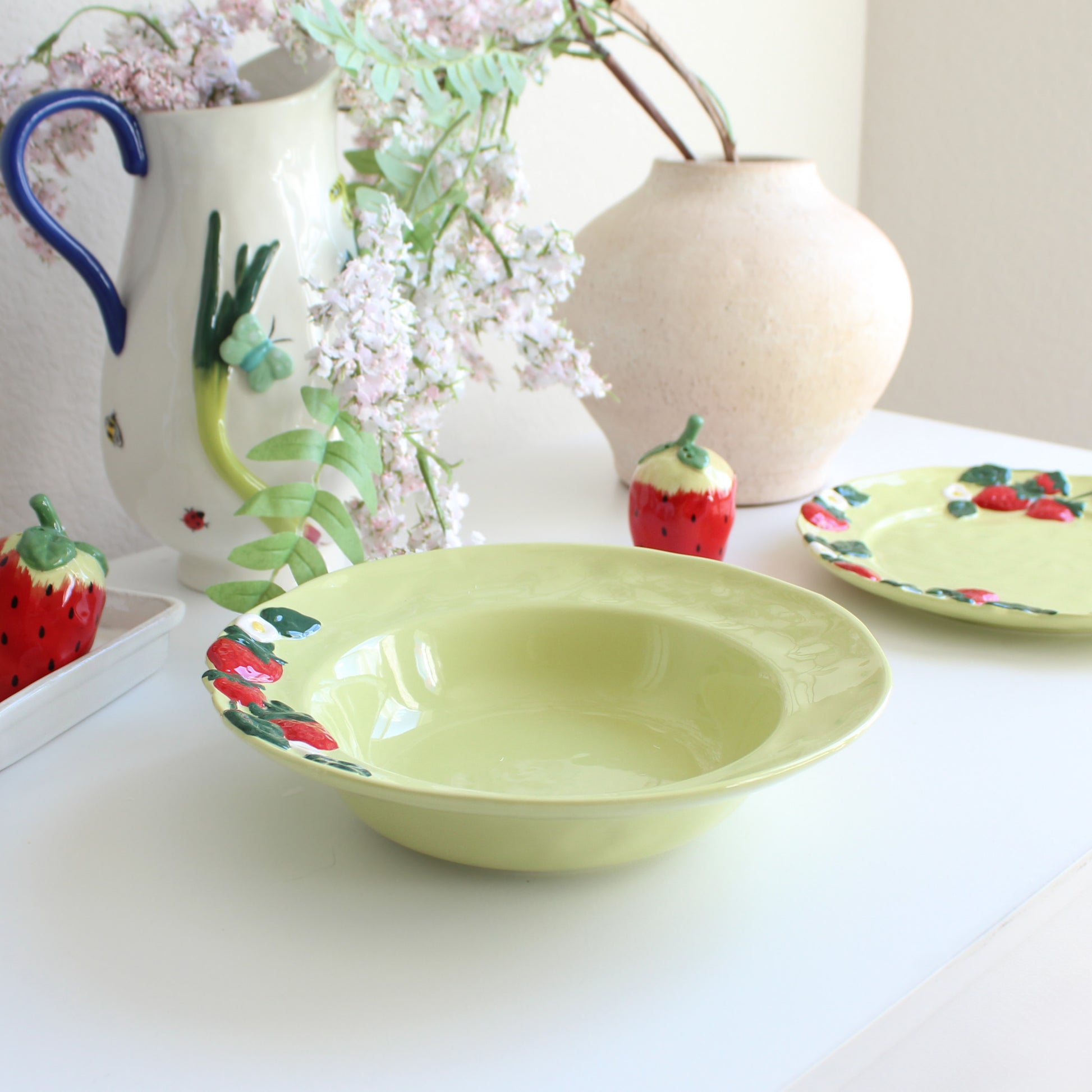 Strawberry-themed handpainted stoneware pasta bowl styled on table with matching dinnerware collection, plate, and salt & pepper shakers