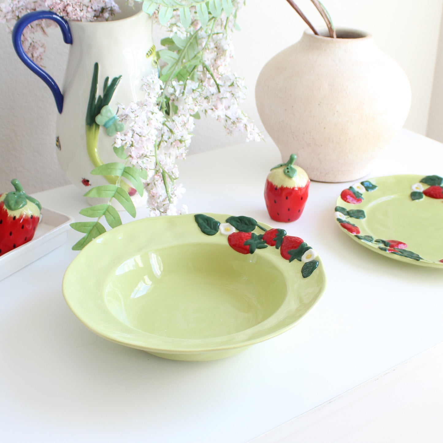 Strawberry-themed handpainted stoneware pasta bowl styled on table with matching dinnerware collection