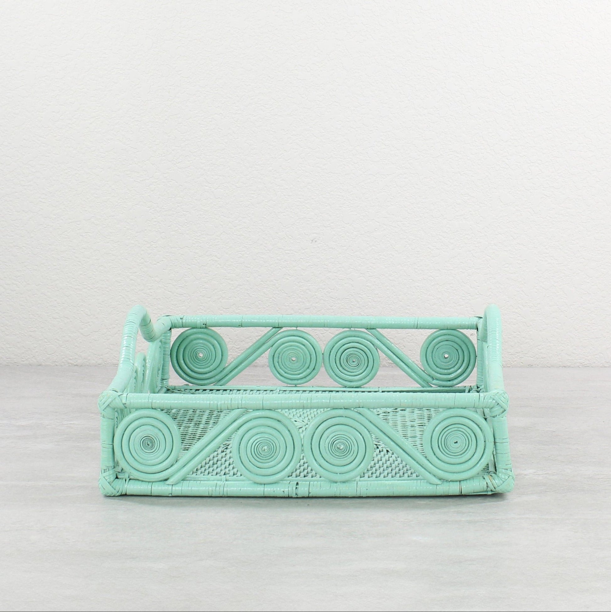 Square sage green rattan tray with swirly edges and curved handle, handwoven for eco-friendly storage.