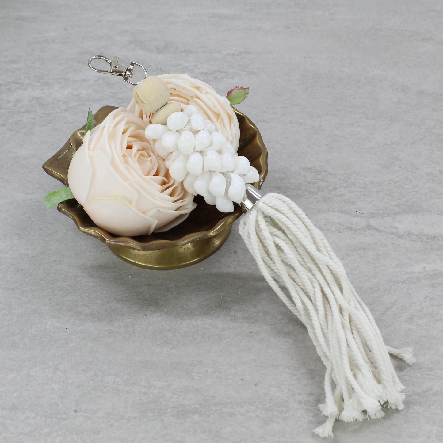 Handmade glossy white seashell key ring with long white cotton fringe tassel displayed in brass dish with soft blush flowers.