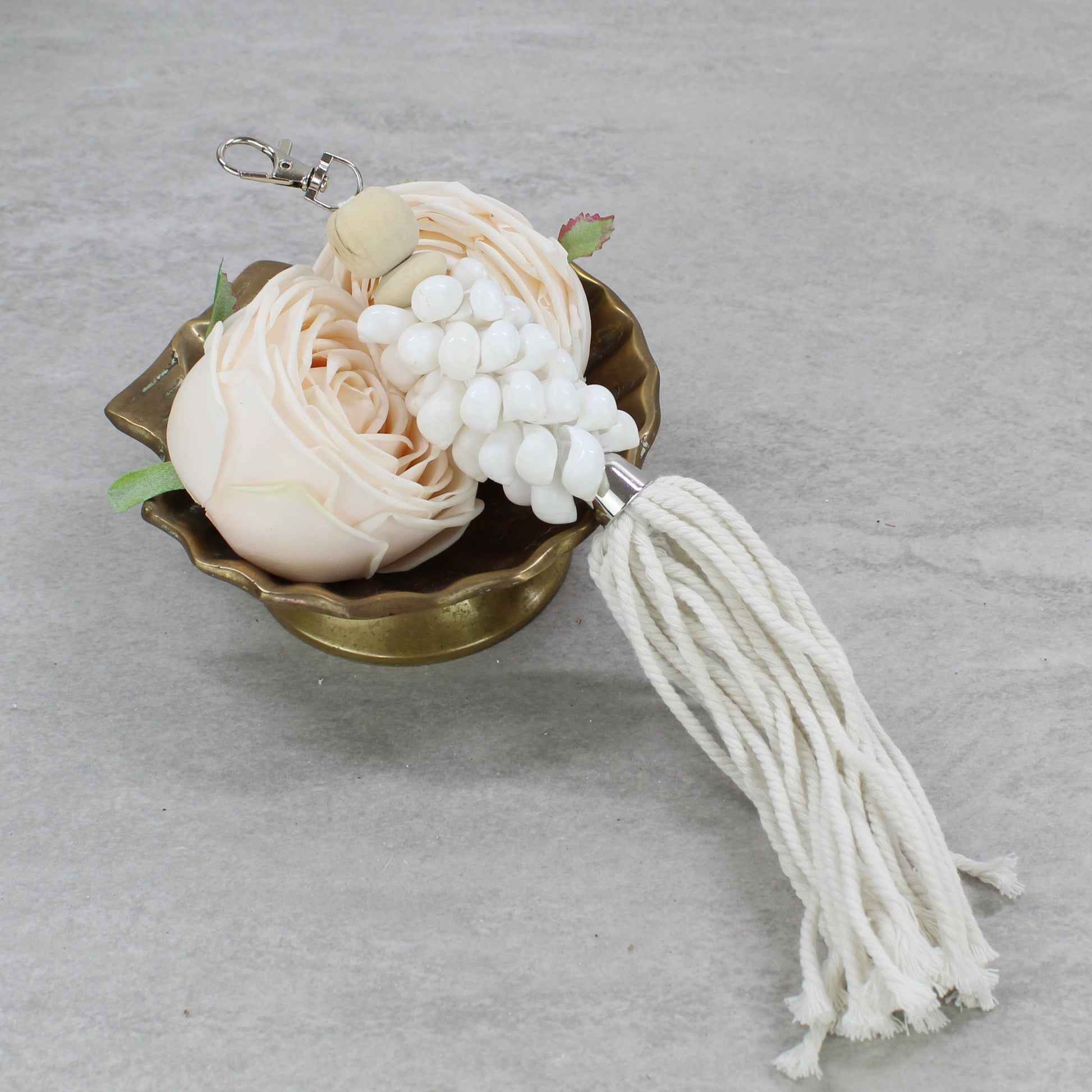 Handmade glossy white seashell key ring with long white cotton fringe tassel displayed in brass dish with soft blush flowers.