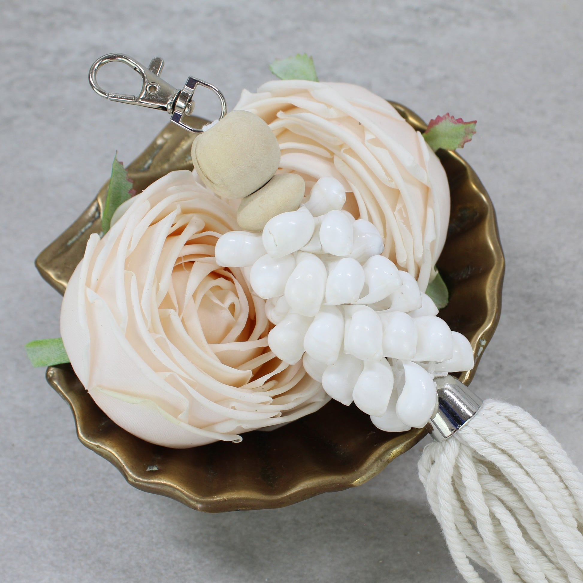 Close-up of glossy white seashell cluster and wooden bead on key ring with cotton tassel, artisan coastal décor detail.