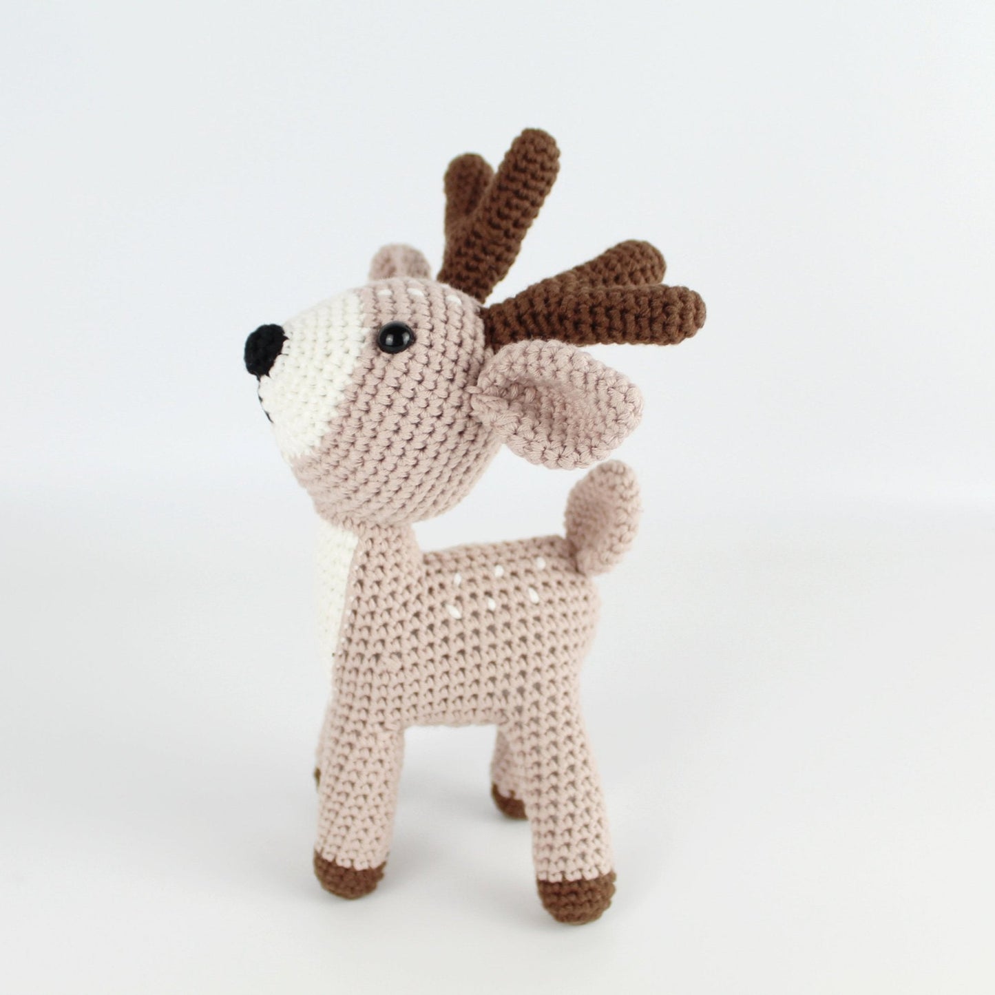 Side view of handmade beige crochet deer amigurumi with brown antlers, eco-conscious and artisanal, designed for holiday gifts or nursery décor.