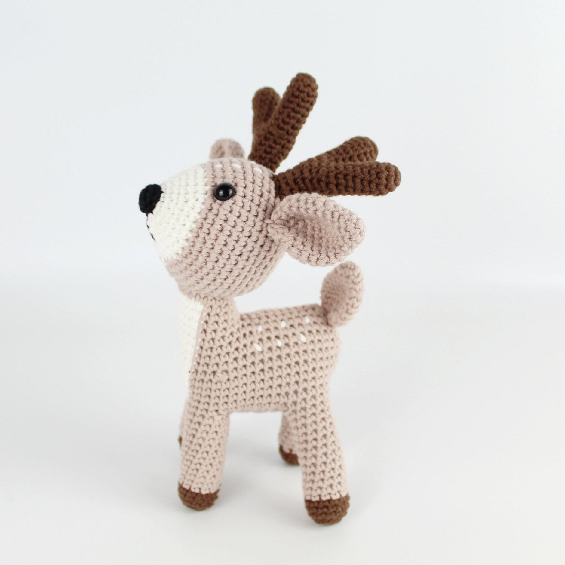 Side view of handmade beige crochet deer amigurumi with brown antlers, eco-conscious and artisanal, designed for holiday gifts or nursery décor.