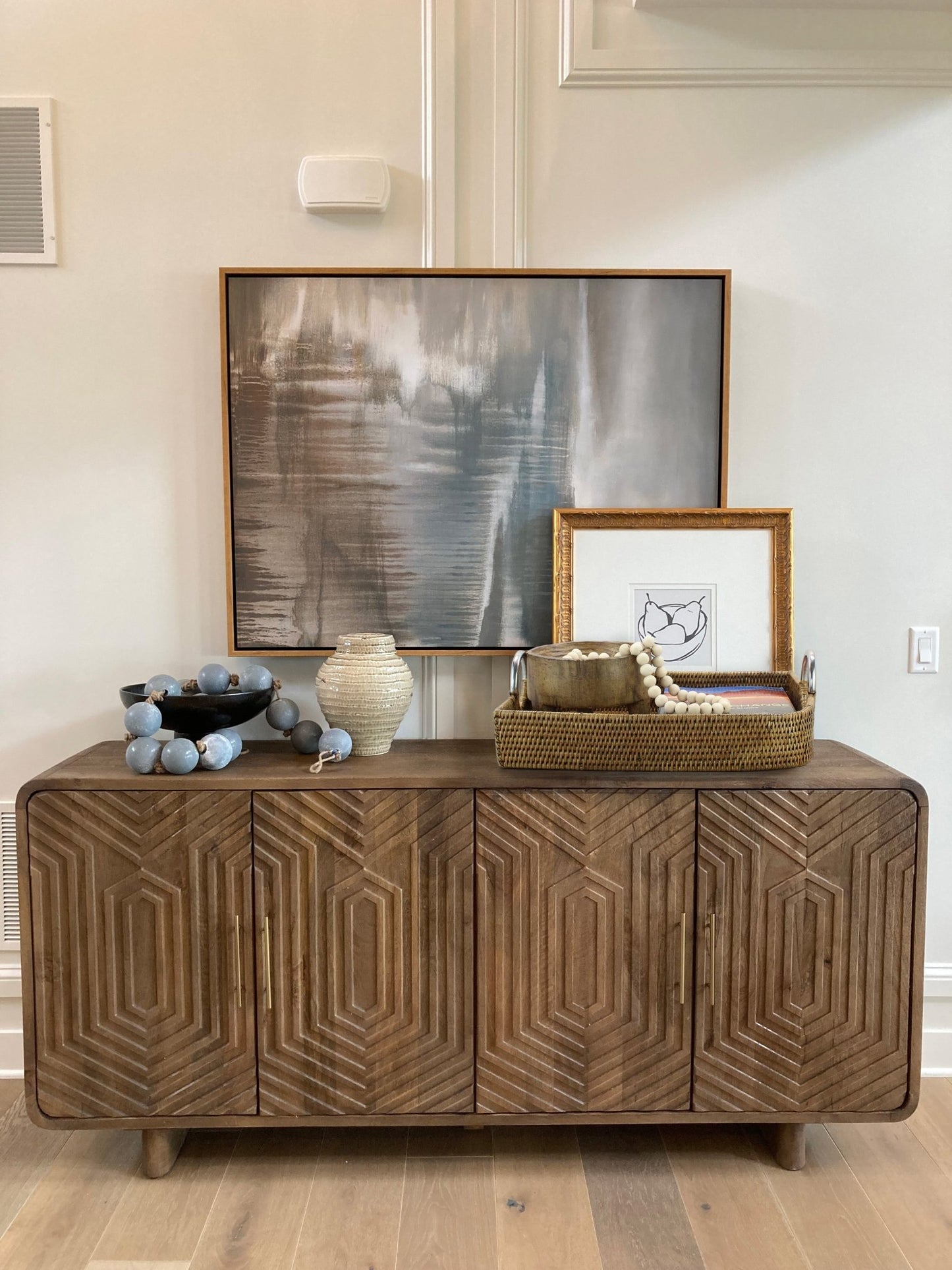 Large leaf shaped honey brown decorative rattan tray with steel handles styled on wood console table with artwork, beads, and vases.