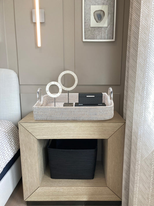 Whitewash large leaf shaped rattan tray with steel handles styled on modern bedside table with books and circular sculptures.