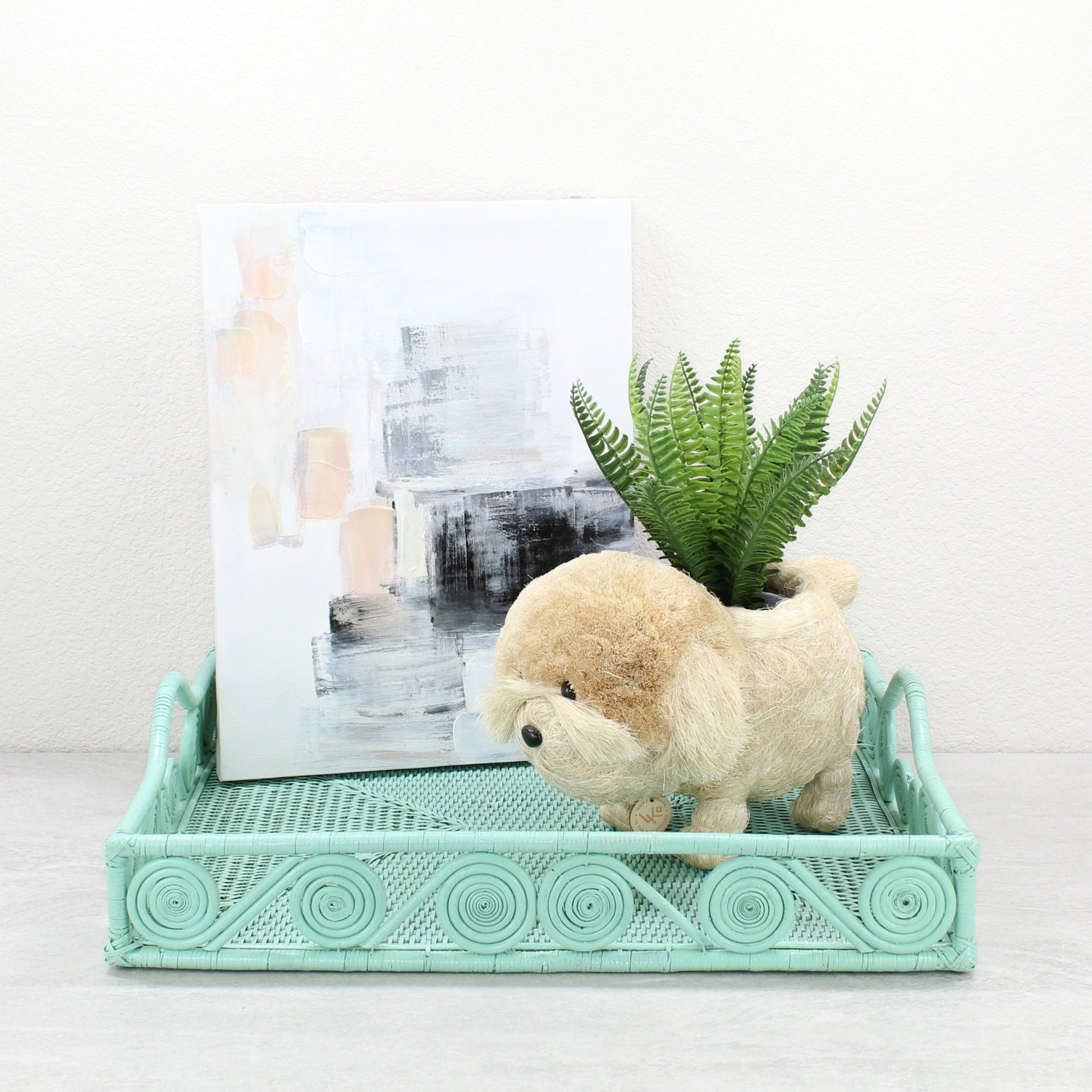 Sage Leaf Green rectangular rattan tray with swirl design styled with abstract artwork and a dog-shaped planter holding a fern for playful home décor.