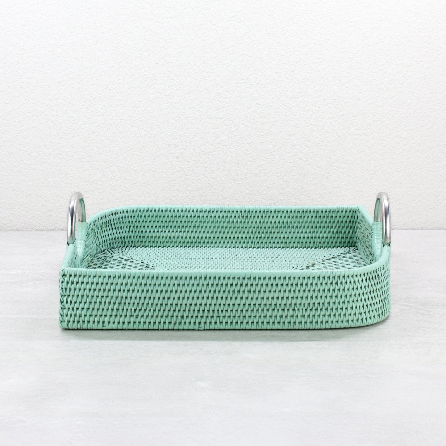 Sage leaf green leaf shaped rattan tray with steel handles shown empty on light surface.