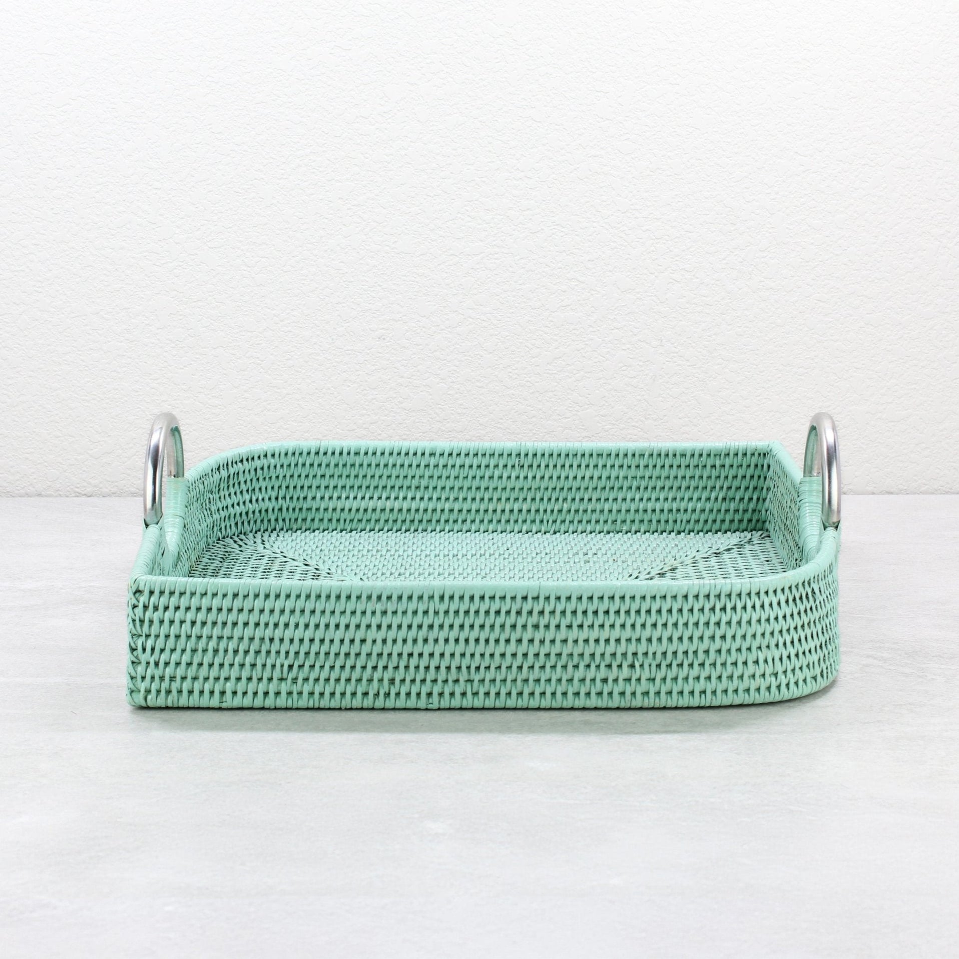 Sage leaf green leaf shaped rattan tray with steel handles shown empty on light surface.