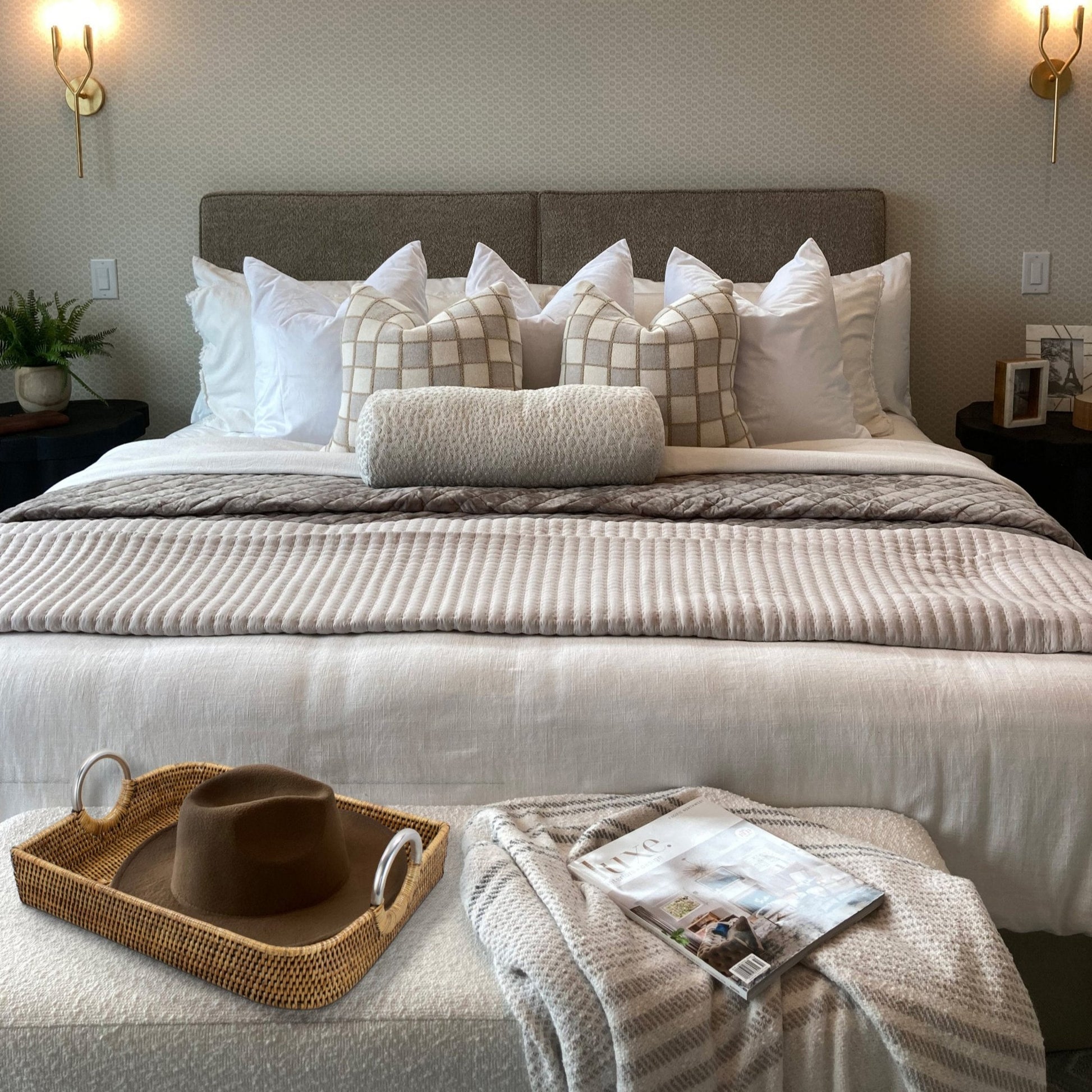 Honey brown small leaf shaped rattan tray placed on bed bench with hat and magazine, styled in cozy neutral bedroom.