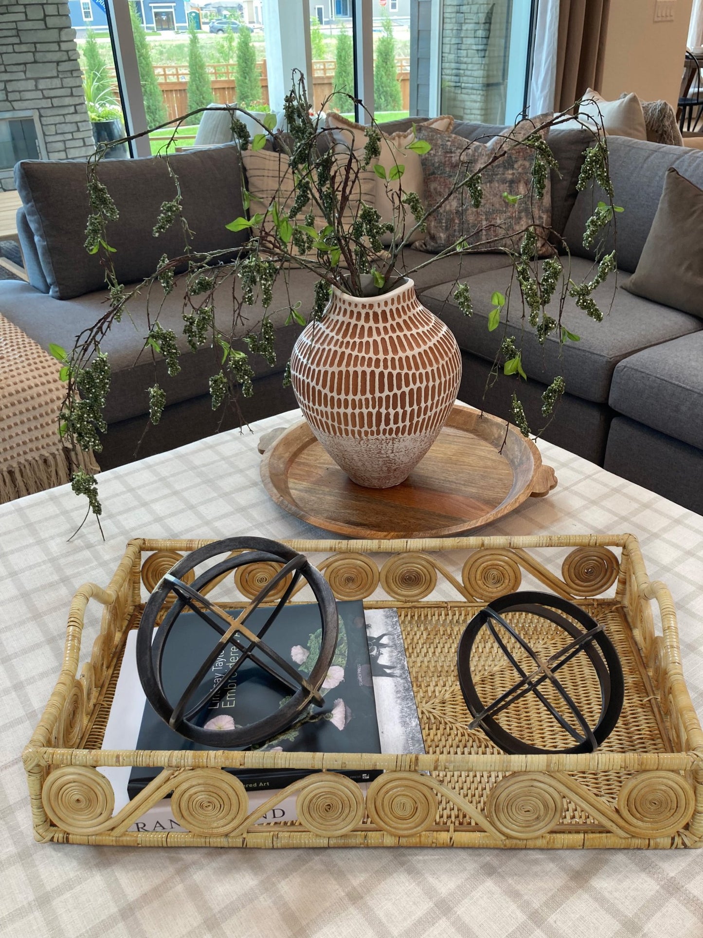 Natural rattan tray on a coffee table holding books and black decorative spheres, styled in a modern living room.