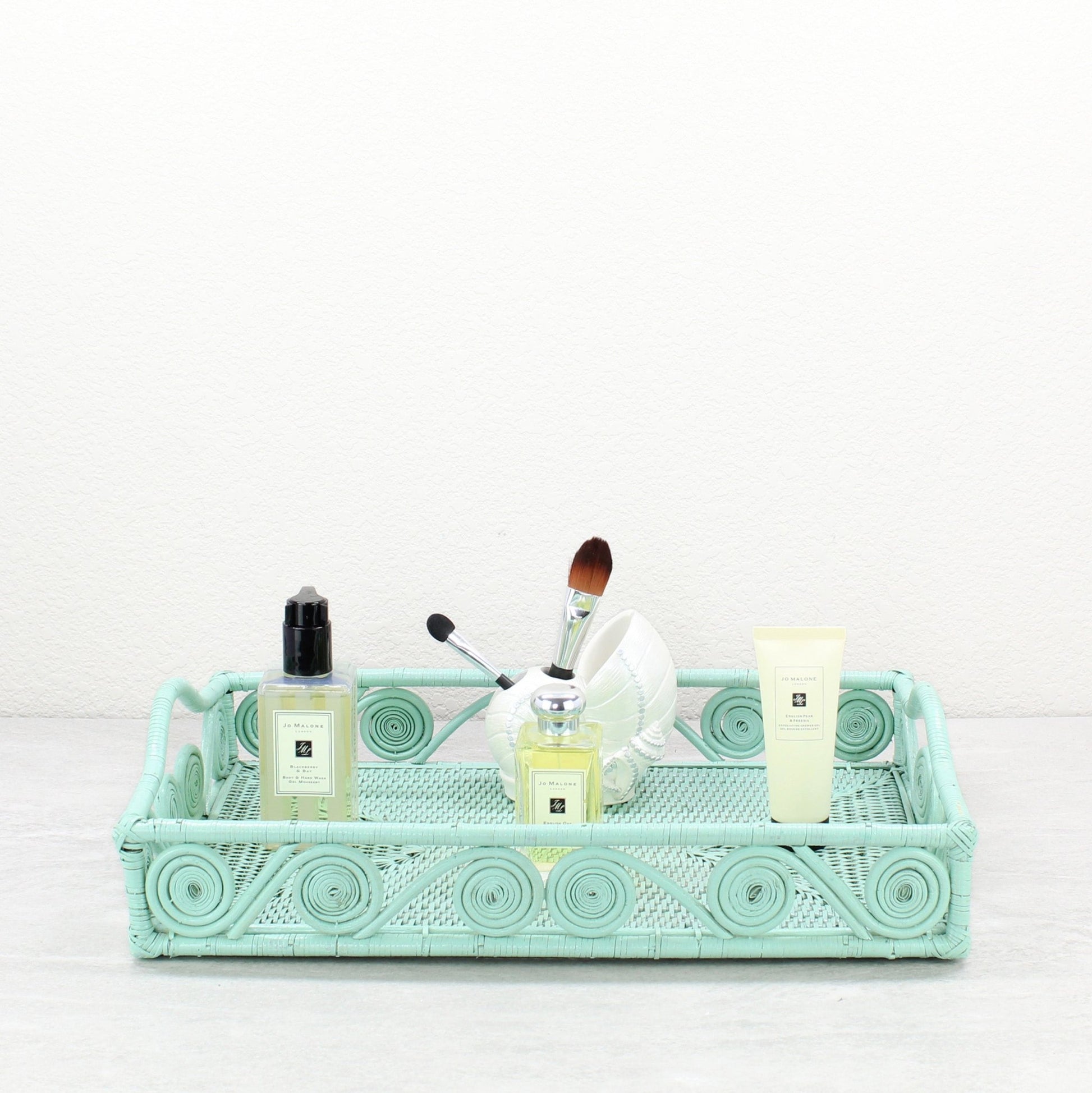 Turquoise rattan tray used for bathroom vanity styling with Jo Malone perfume, lotion, and a seashell brush holder.