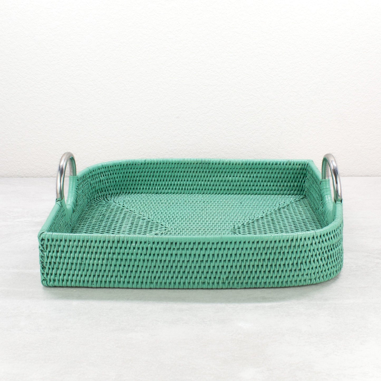 Turquoise leaf shaped rattan tray with steel handles shown empty on light surface.