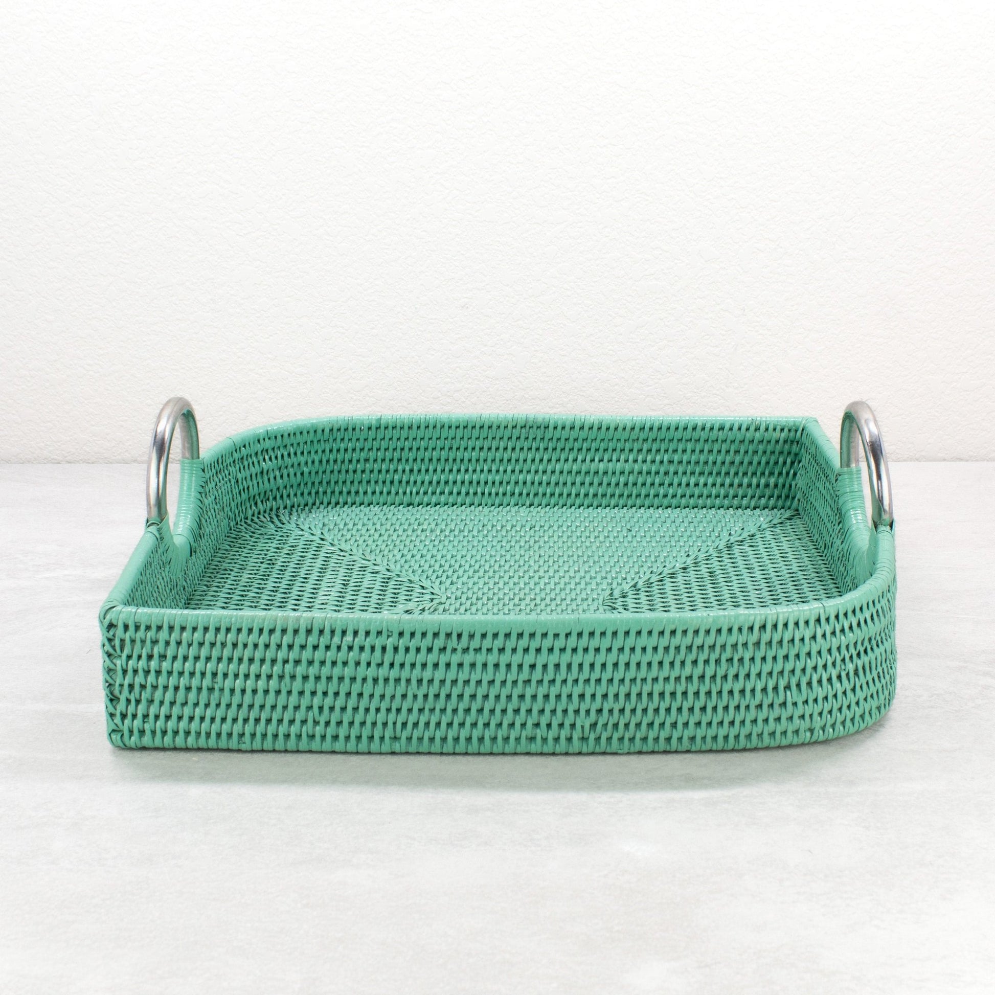 Turquoise leaf shaped rattan tray with steel handles shown empty on light surface.