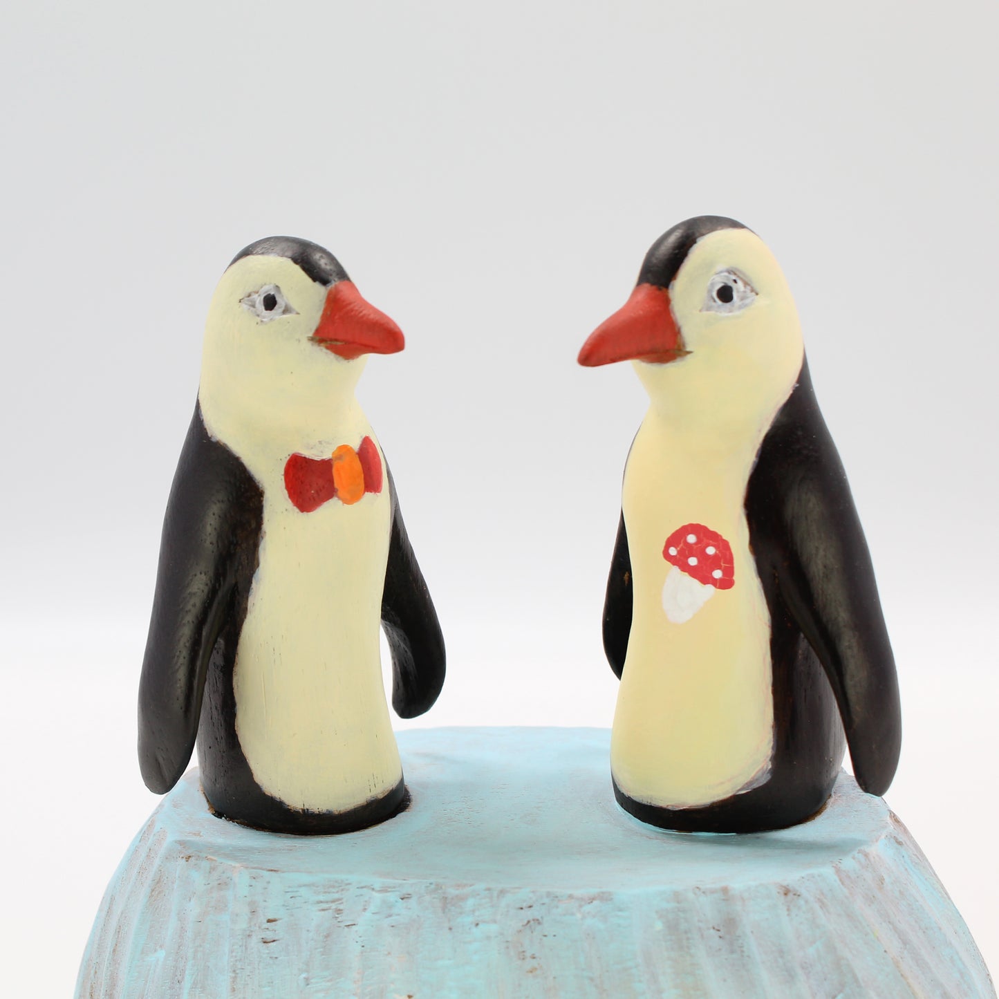 Pair of hand-painted wooden penguin sculptures with bow tie and mushroom detail, eco-conscious artisan décor figurines, close view