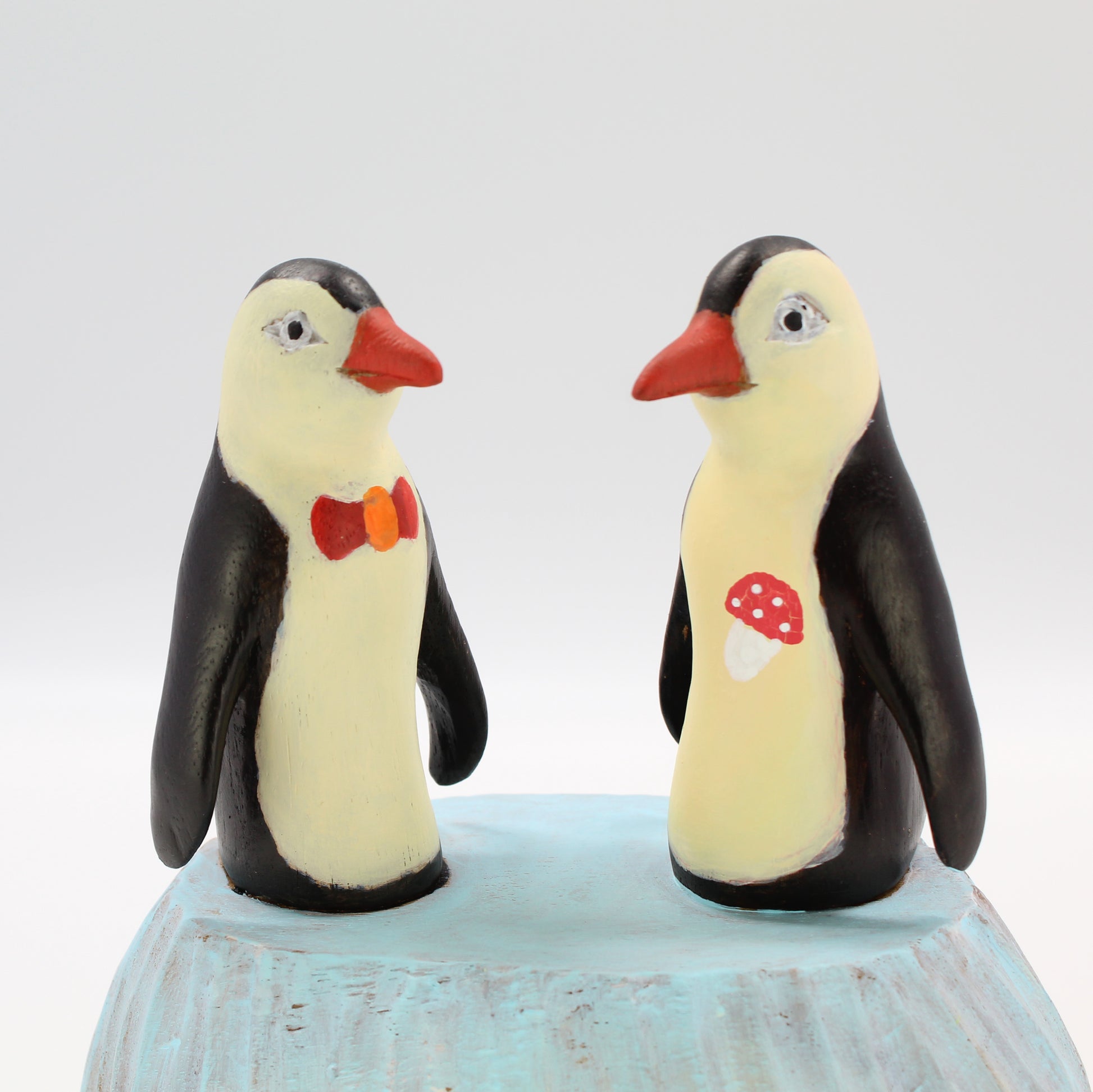 Pair of hand-painted wooden penguin sculptures with bow tie and mushroom detail, eco-conscious artisan décor figurines, close view