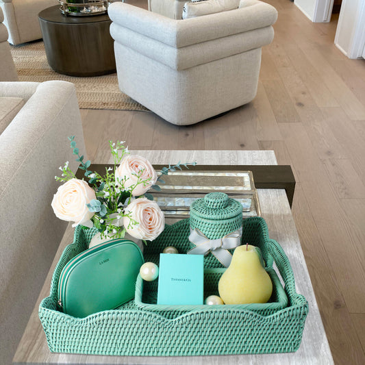 Handwoven sage leaf green rattan tray styled as a wedding or holiday gift with flowers, canister, and accents on a modern living room side table