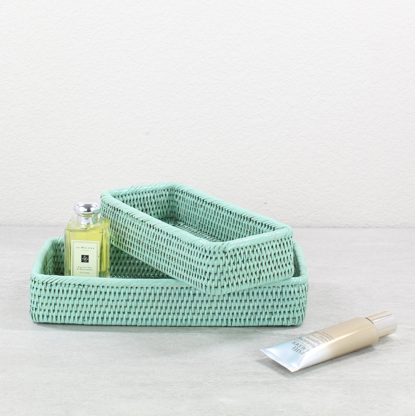 Eco-friendly sage green rattan bathroom tray set, tight-woven rectangular baskets styled with luxury skincare products