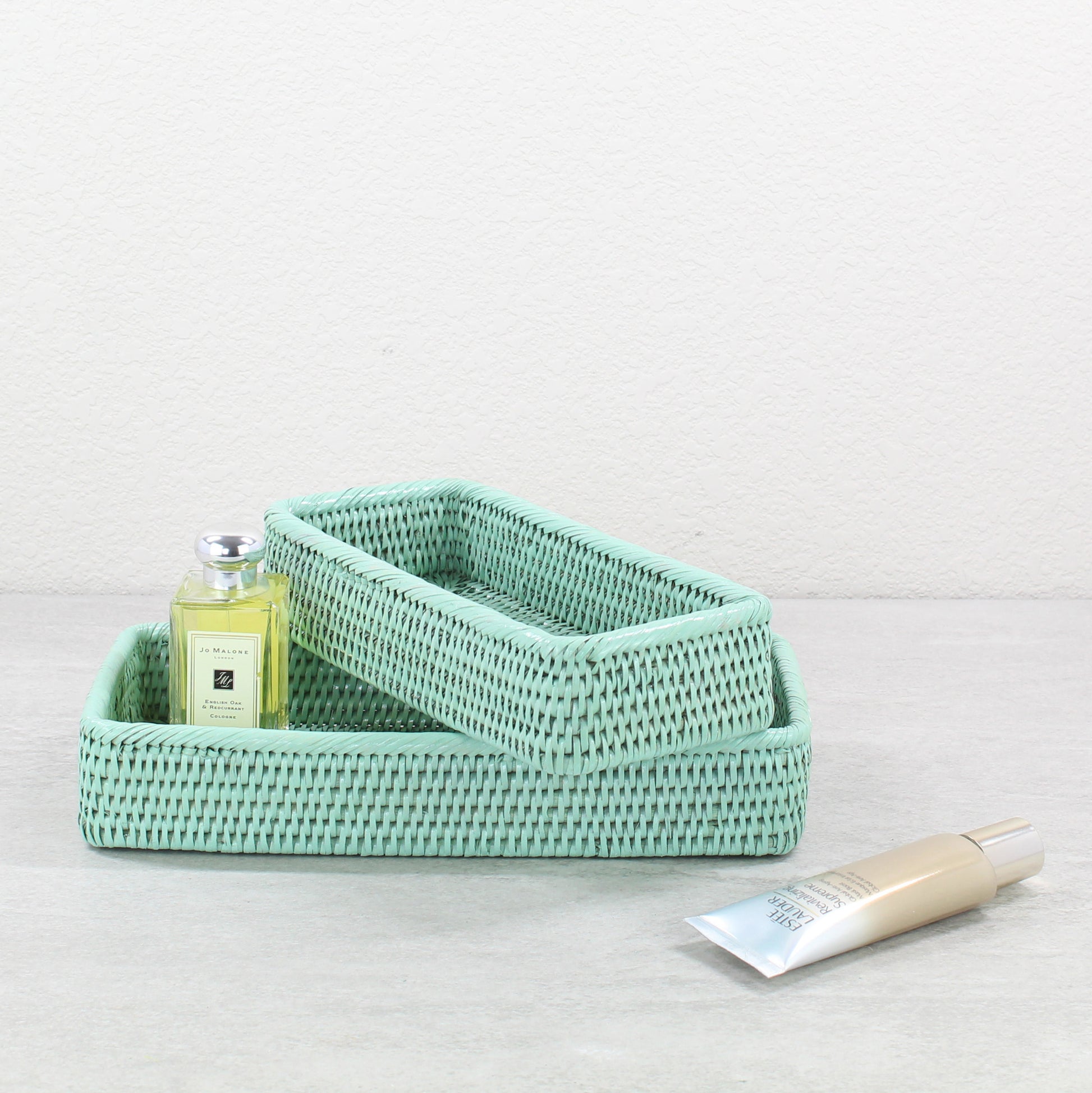 Eco-friendly sage green rattan bathroom tray set, tight-woven rectangular baskets styled with luxury skincare products