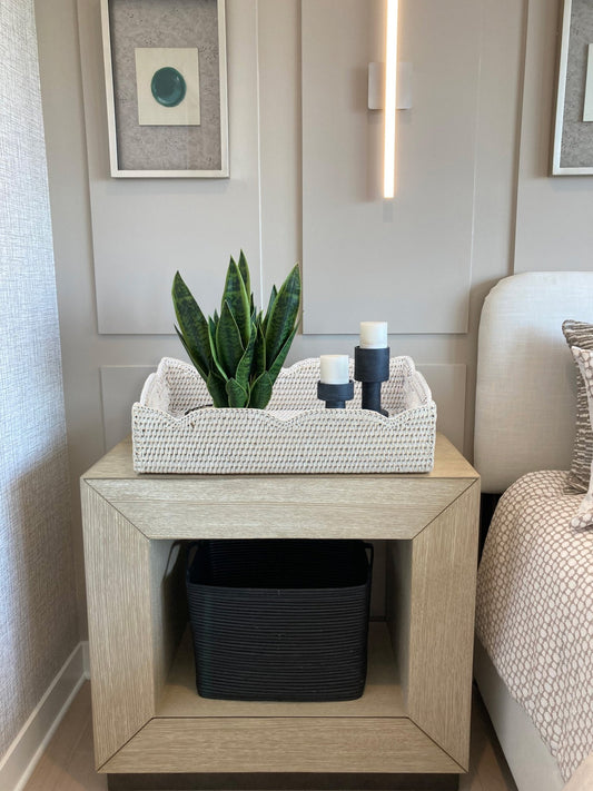 Whitewash medium scalloped rattan tray with handles styled on a bedroom nightstand holding a plant and candles.