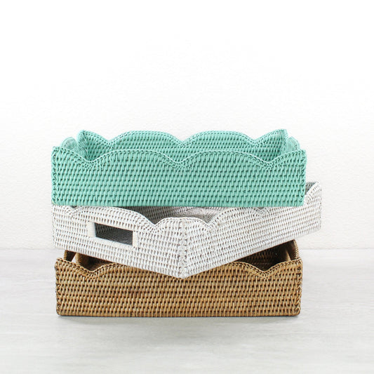 Handwoven scalloped edge rattan trays with handles in turquoise, whitewash, and honey brown stacked together.