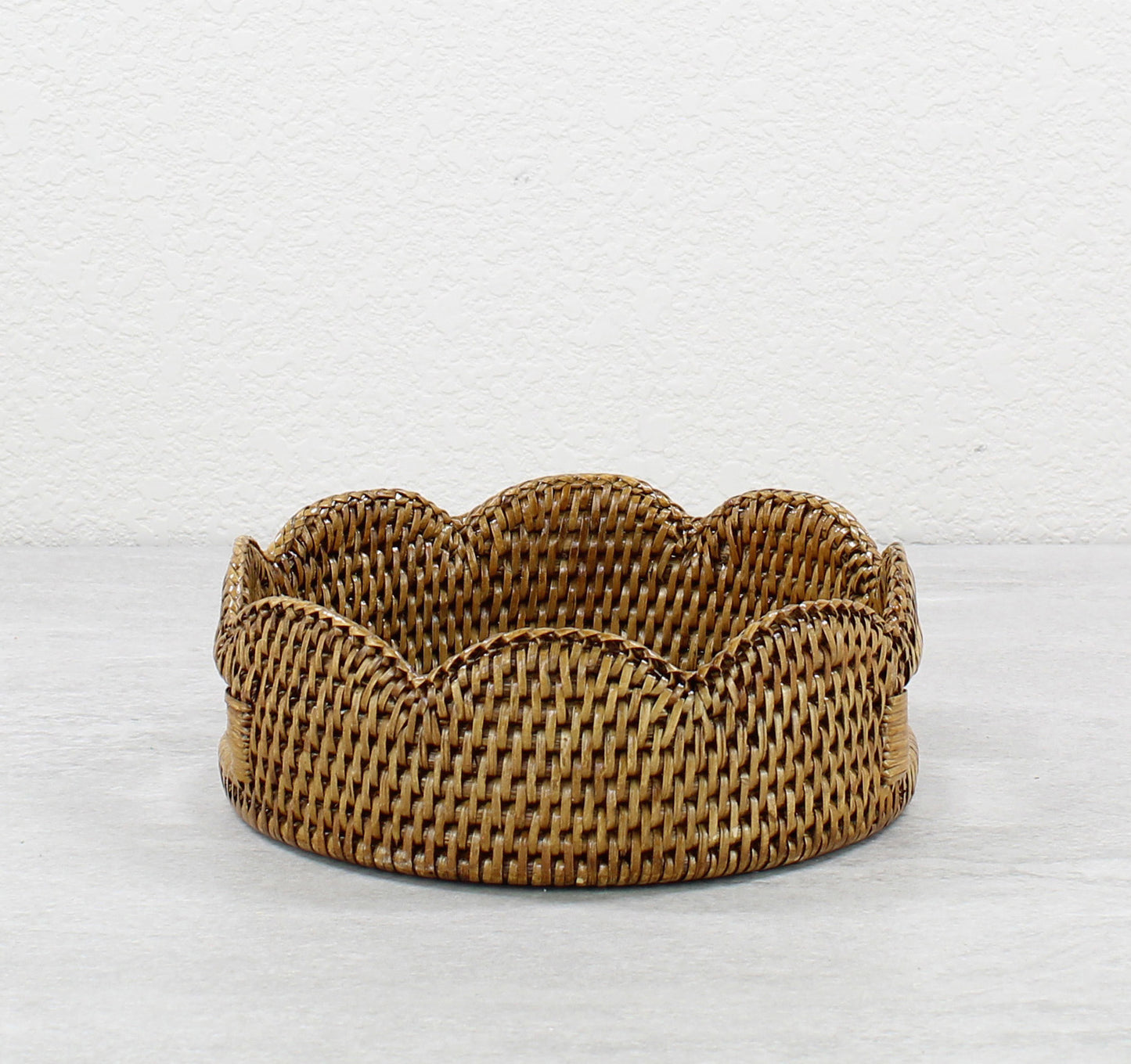 Front view of small scalloped round rattan tray in honey brown, handmade artisan storage basket or serving tray
